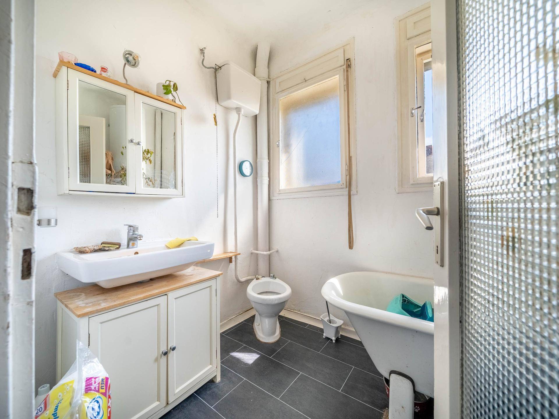 Modernisiertes Badezimmer mit dunklen Fliesen, Waschtisch und Badewanne.