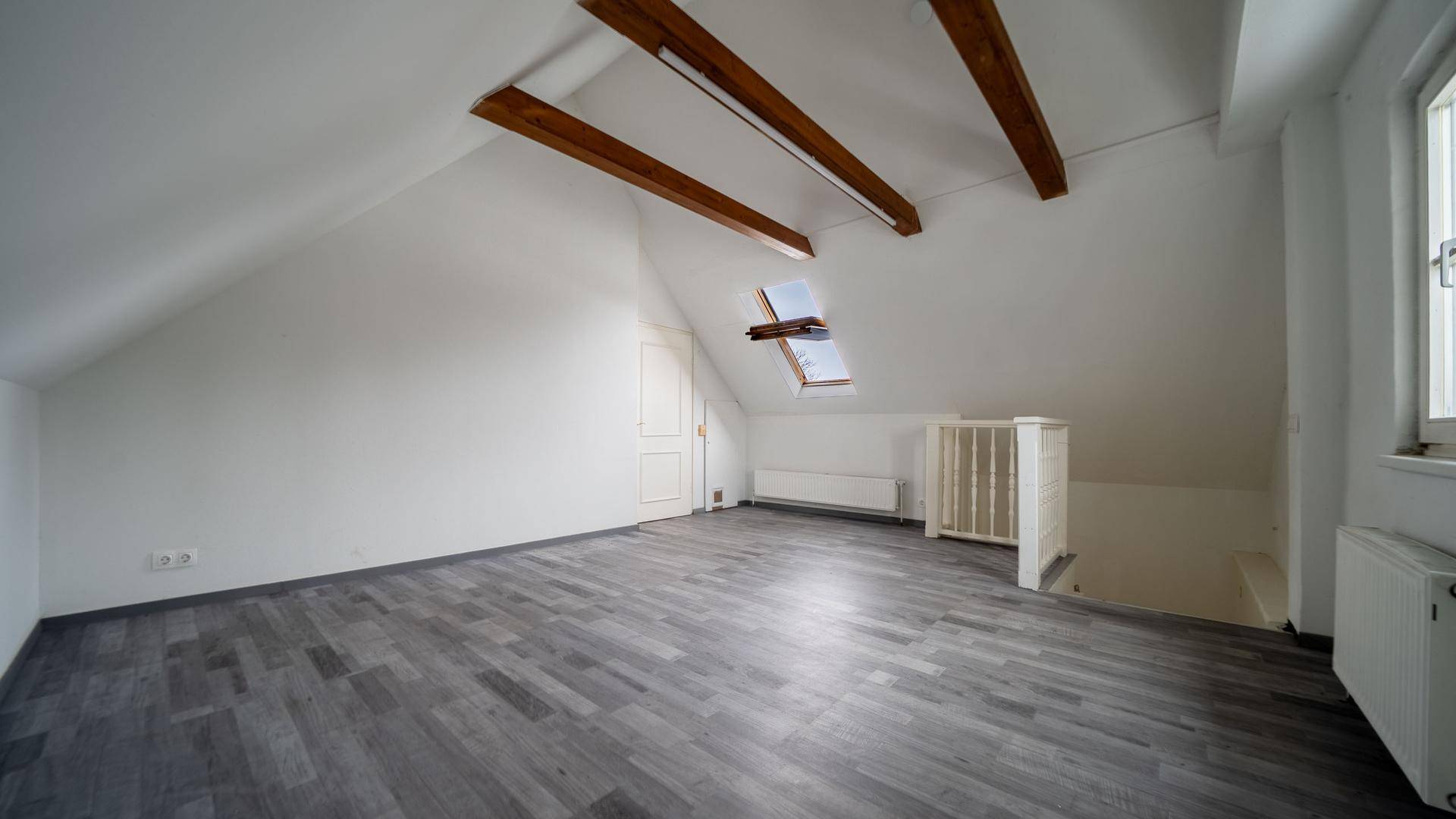 Geräumiges Dachzimmer mit sichtbaren Holzbalken, Dachfenster und Laminatboden, ideal als Schlafzimmer.