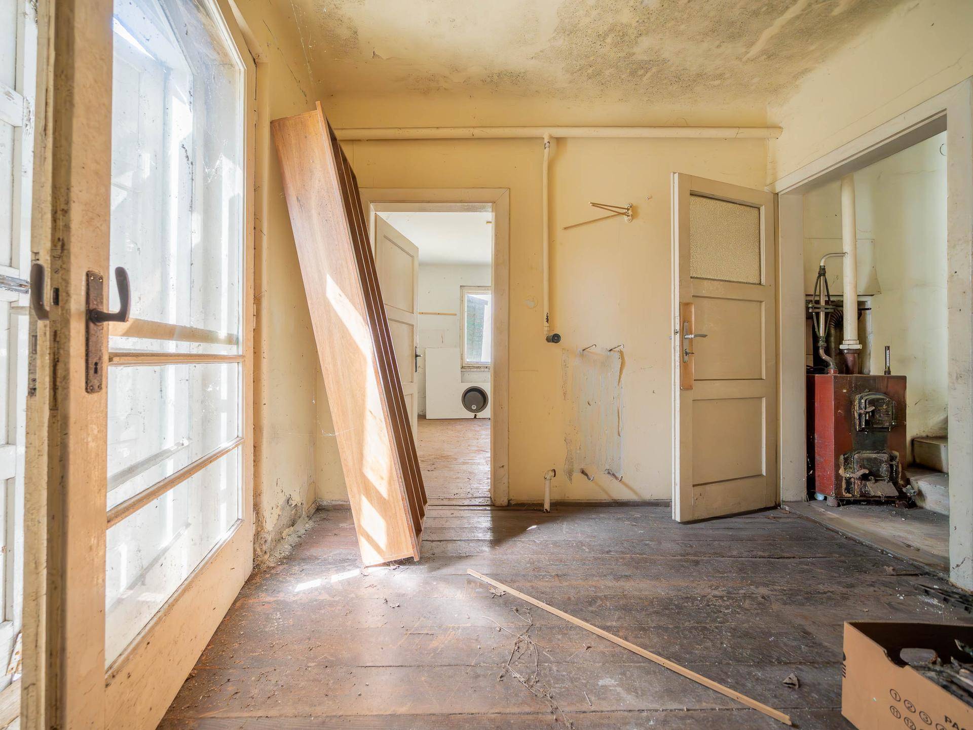 Abgenutzter Raum mit Holzboden und Tür zu einem weiteren Bereich, der Renovierung benötigt.