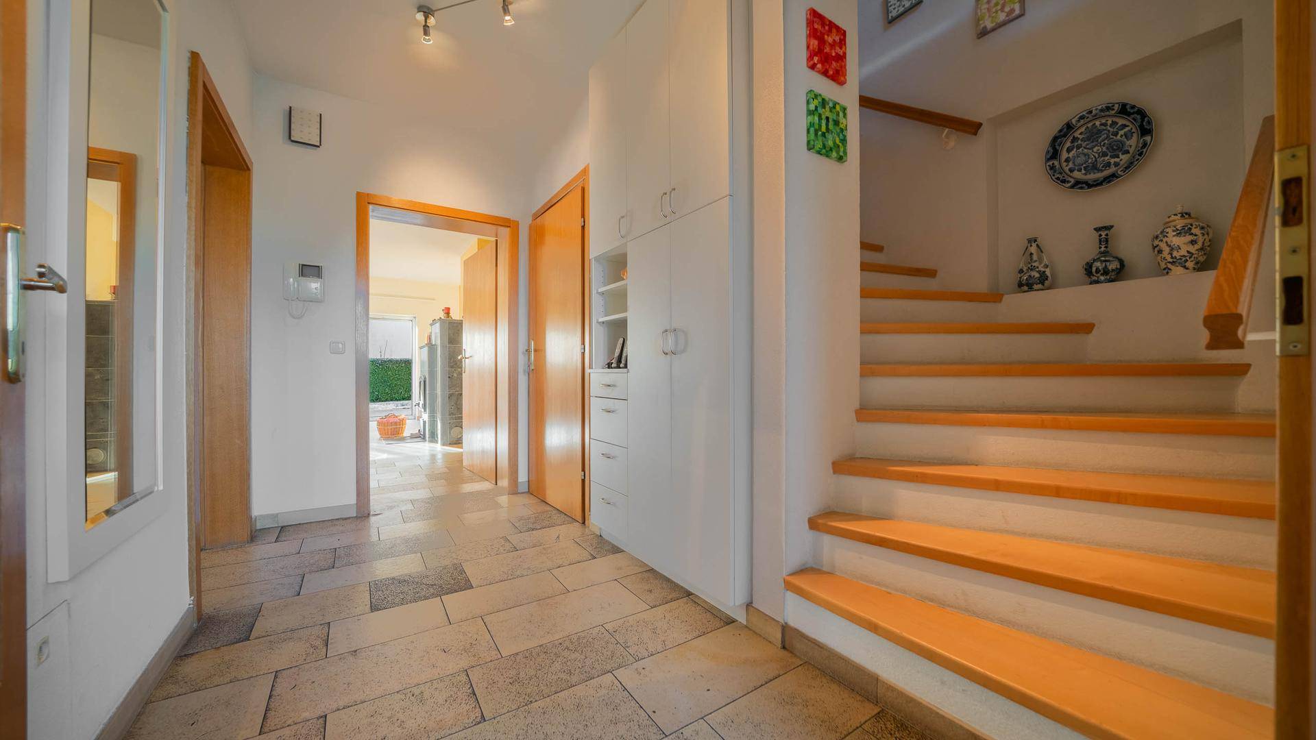 Heller Eingangsbereich mit Fliesenboden, Holztreppe und integrierten Schränken.
