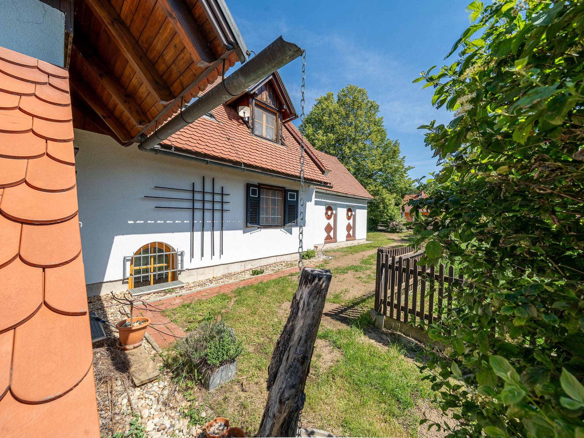 Seitenansicht des Hauses mit kleinem Gartenbereich, Holzzaun und Dachrinne.