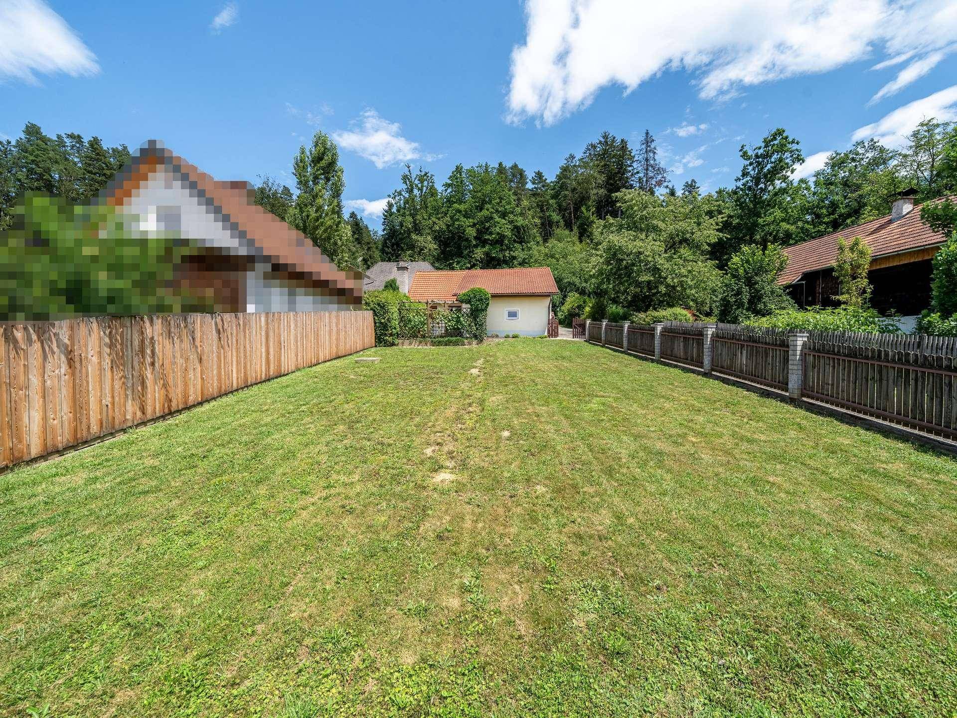 Große, sonnige Rasenfläche im Garten mit Holzzäunen und Blick auf das Haus.