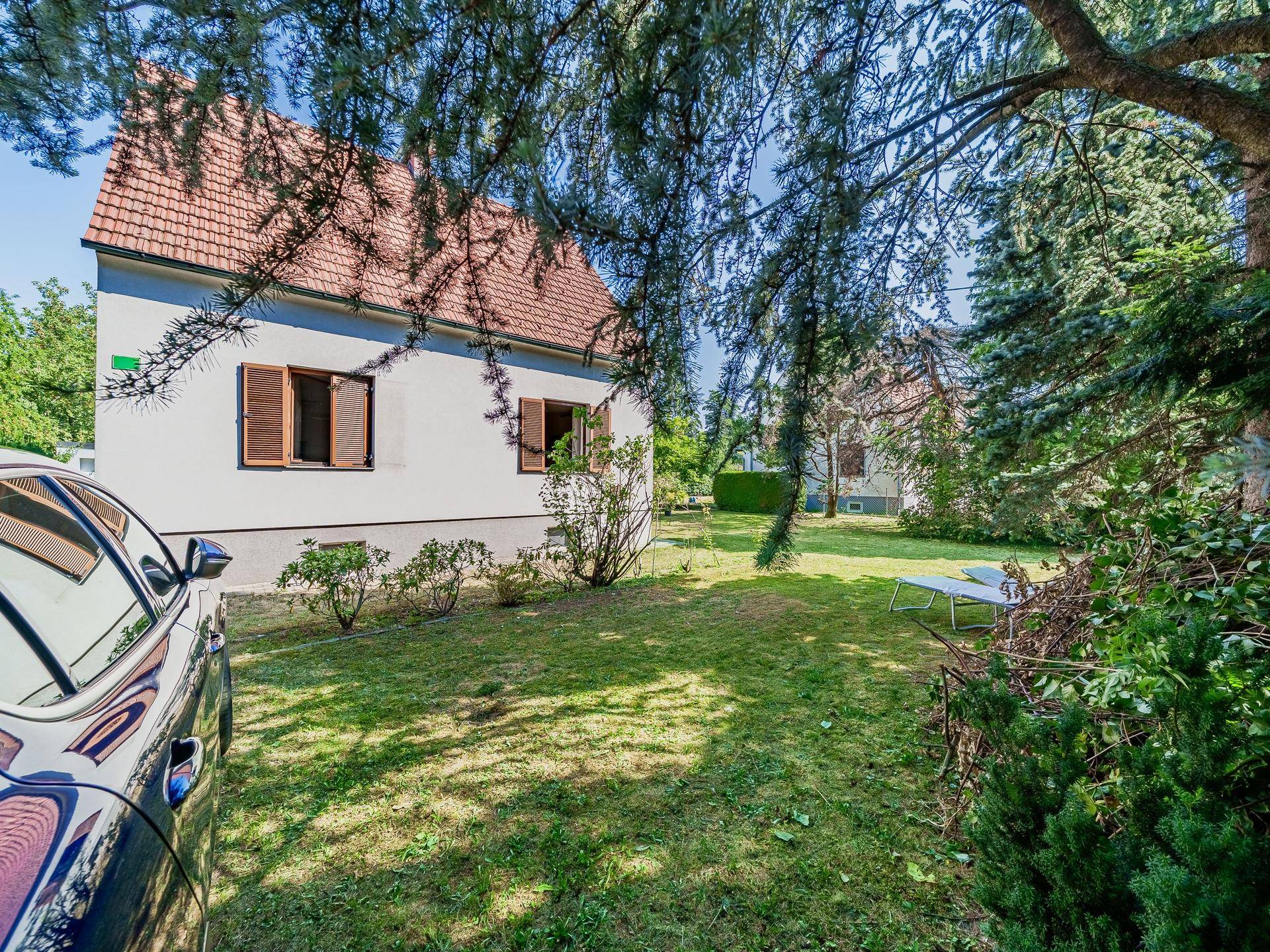 Seitenansicht des Hauses mit Garten und einem geparkten Auto im Vordergrund.