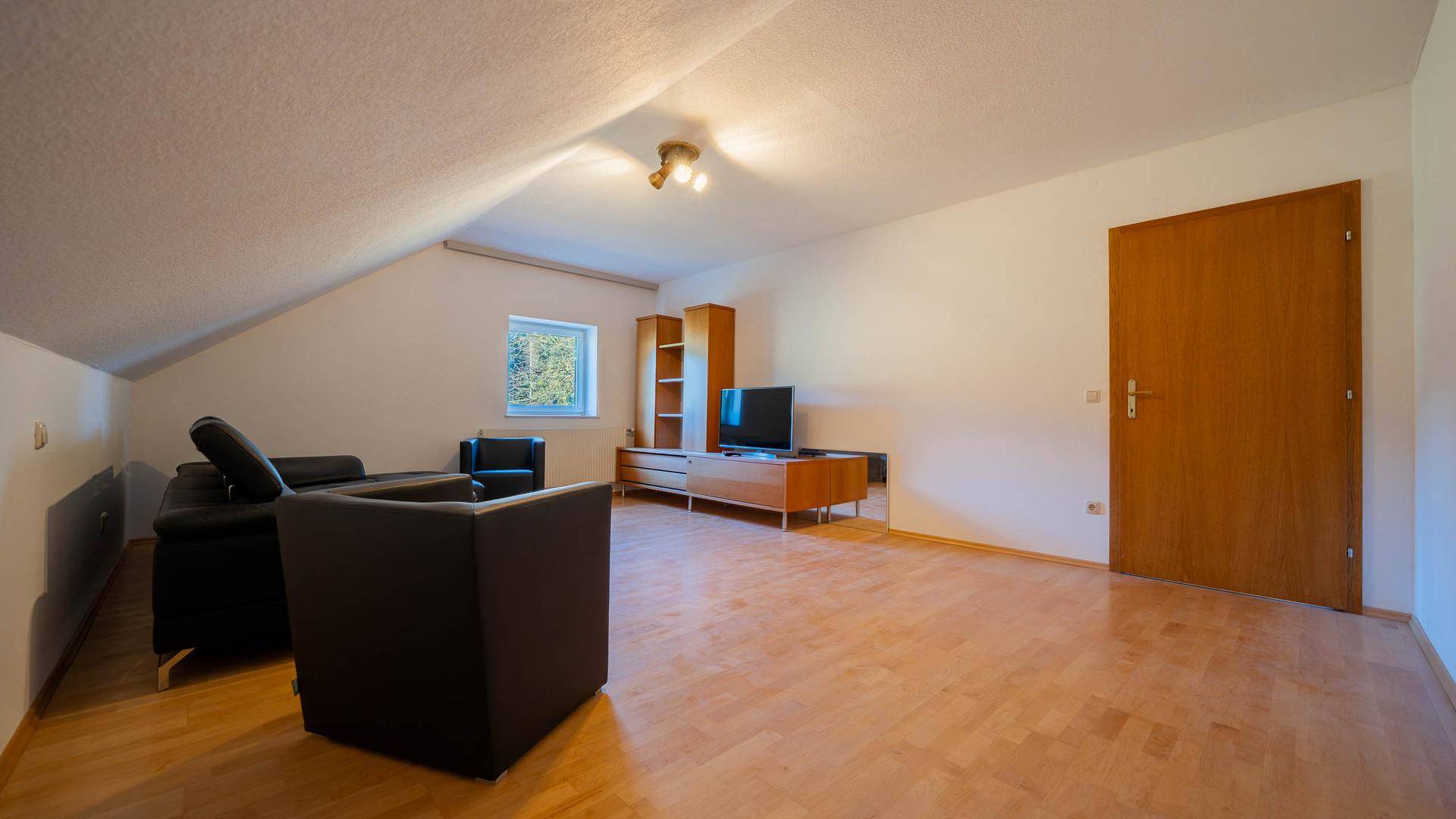 Wohnzimmer im Dachgeschoss mit Holzboden, Dachschräge und bequemer Ledercouch.