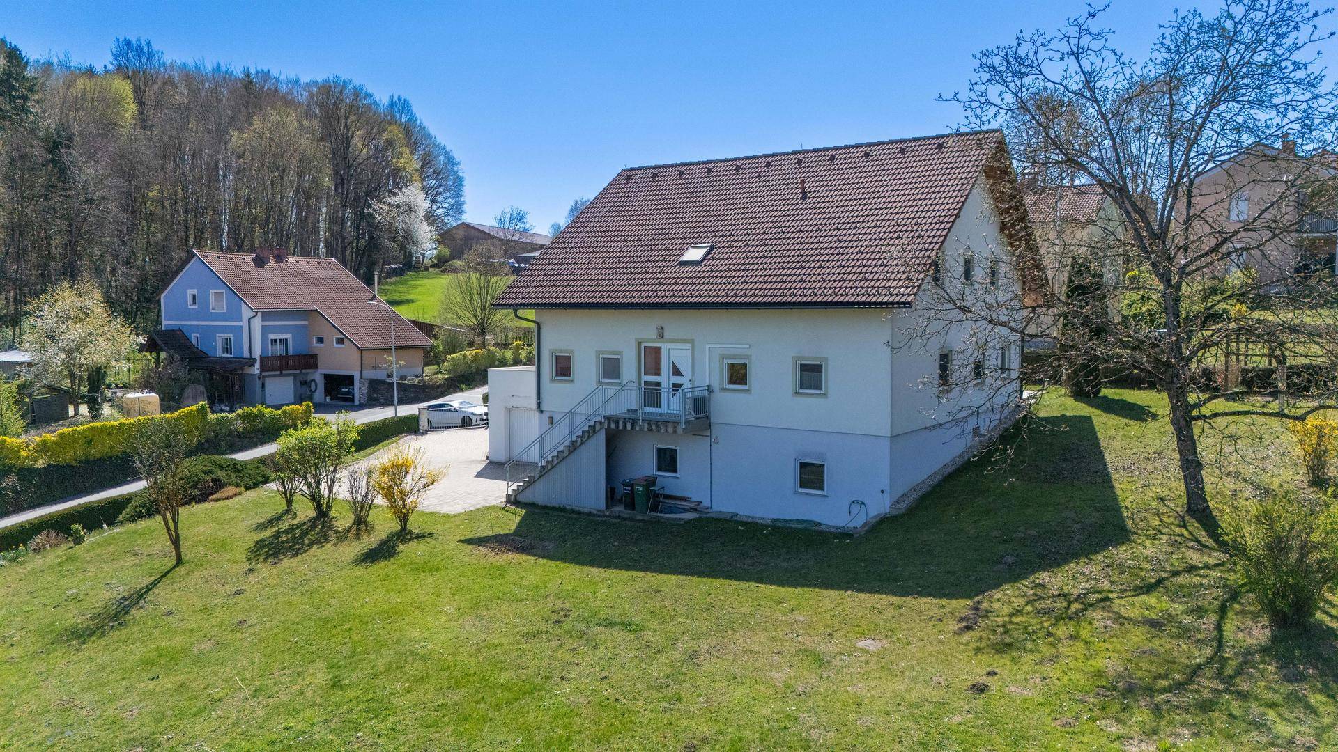 Freistehendes Einfamilienhaus mit weißer Fassade, braunem Dach und Zugangstreppe im Grünen.