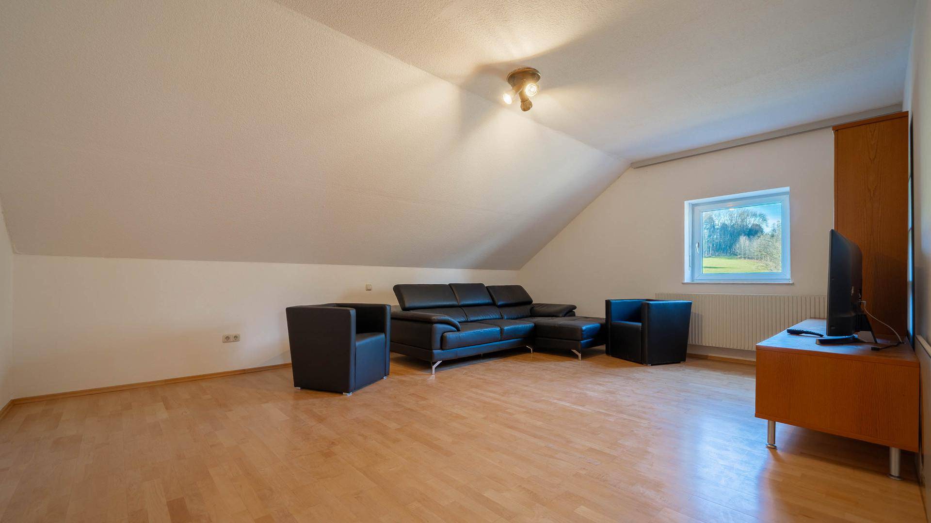 Helles Wohnzimmer im Dachgeschoss mit Holzboden, Dachschräge und Blick ins Grüne.