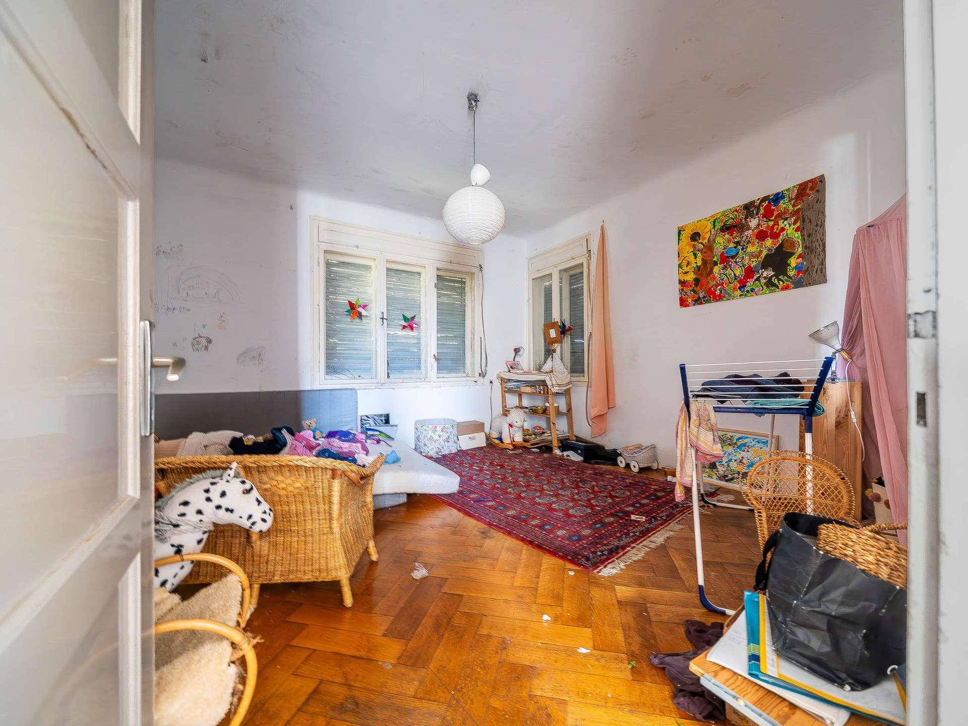 Kinderzimmer mit Parkettboden, bunten Bildern und Fenster, das eine Renovierung benötigt.