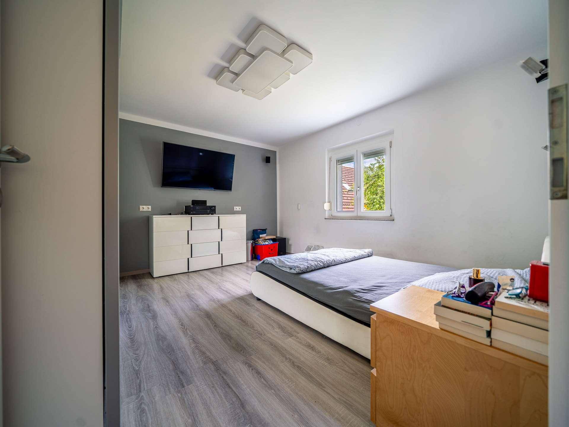 Modernes Schlafzimmer mit Doppelbett, Kommode und Wandfernseher.