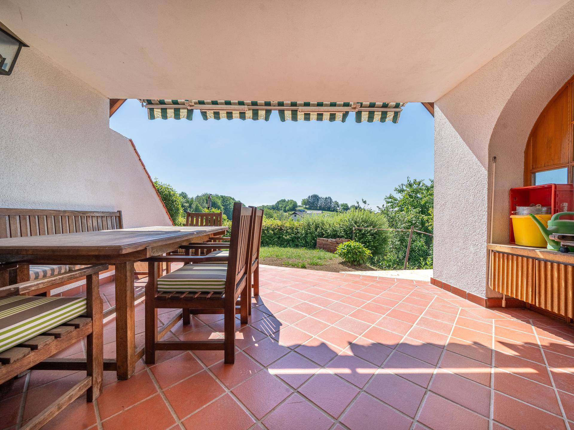 Überdachte Terrasse mit Terrakotta-Fliesen, Gartenmöbeln und weitem Blick ins Grüne.