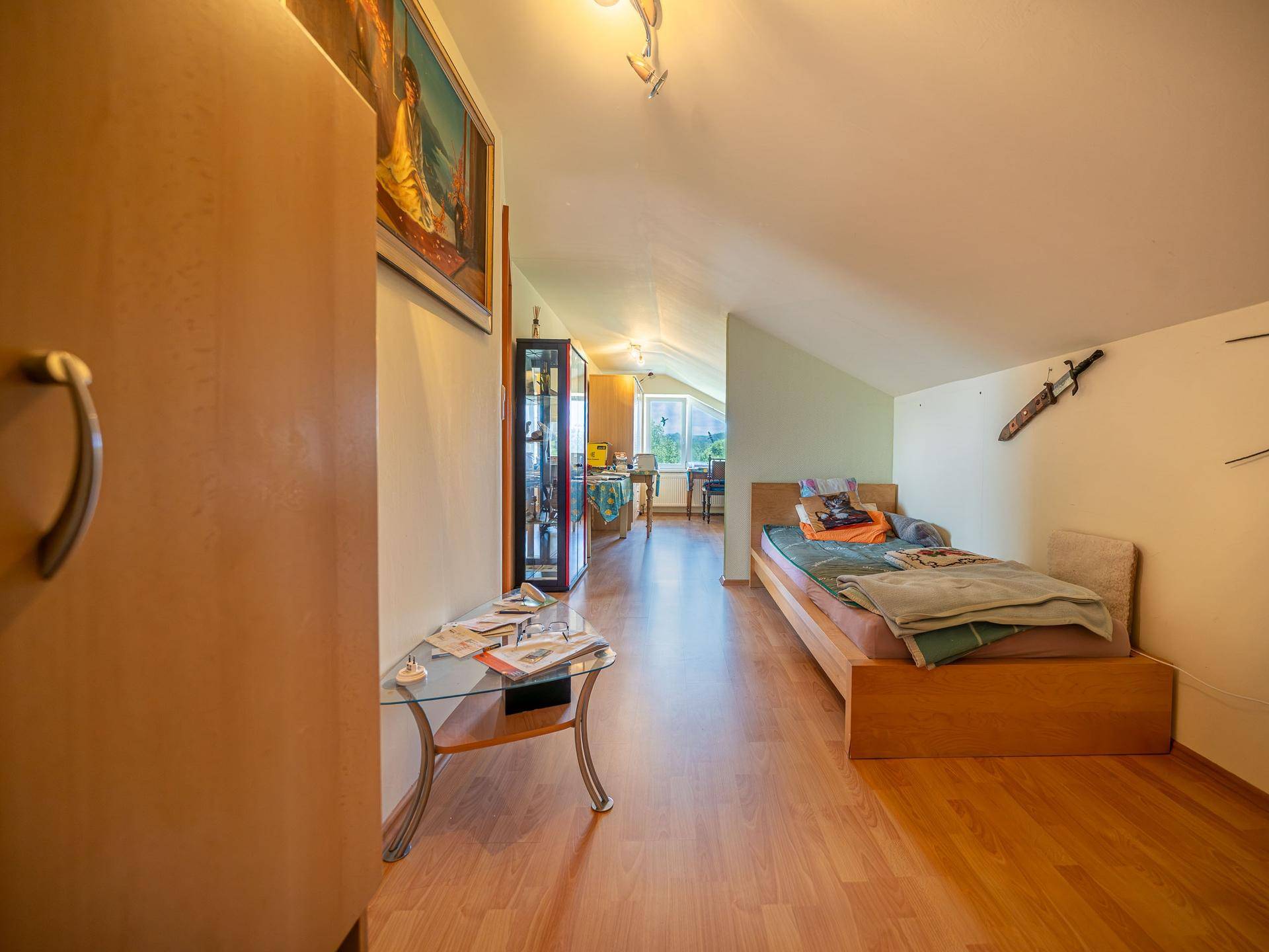 Gemütlicher Dachgeschossraum mit Laminatboden, Bett und schrägen Wänden.