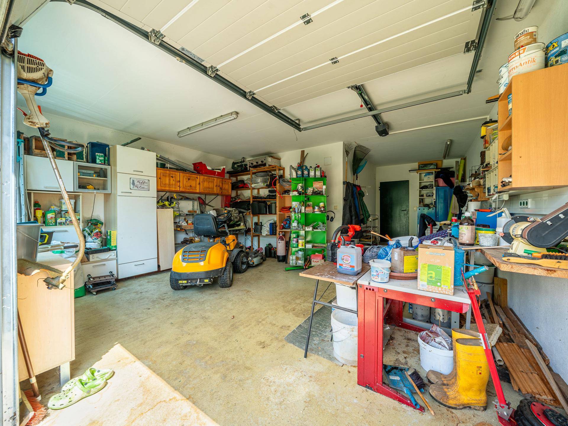 Geräumige Garage mit offenem Tor, Rasenmäher und viel Stauraum für Werkzeuge.