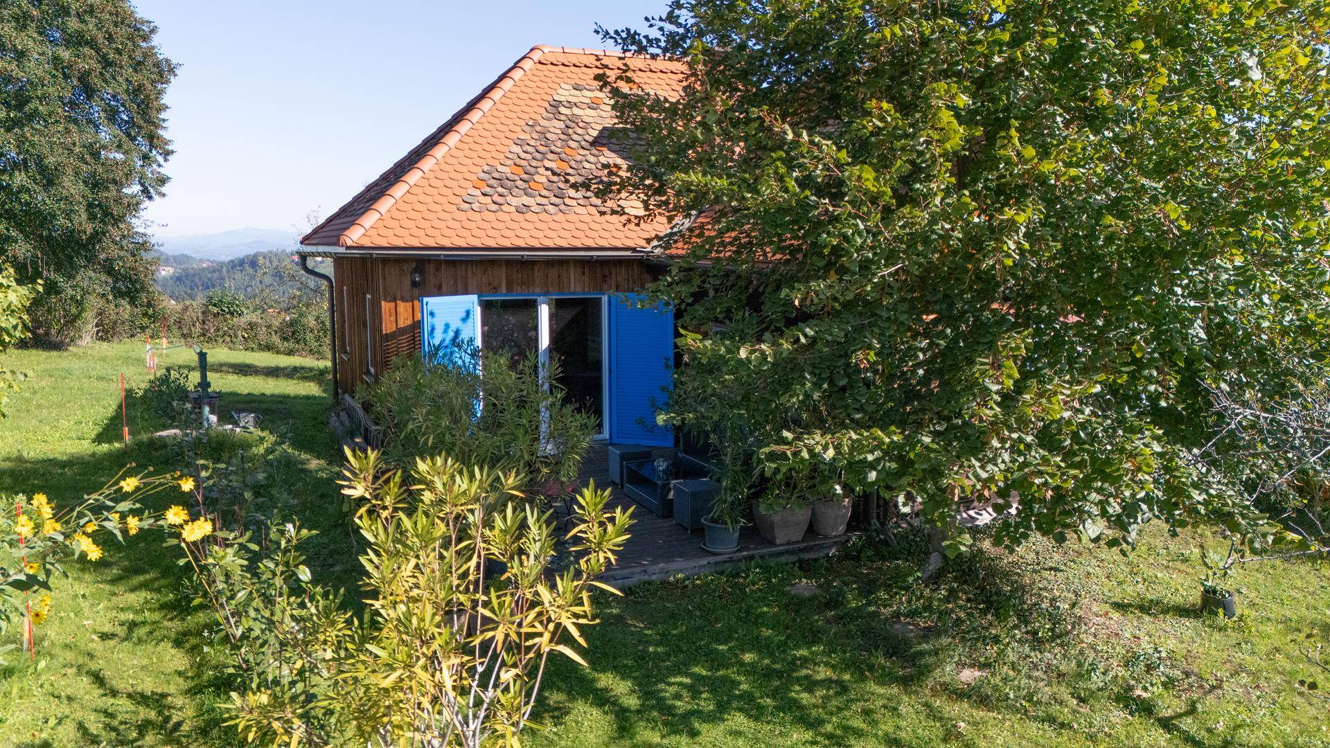 Holzhaus mit Garten und grüner Umgebung aus der Vogelperspektive, eingebettet in die Natur.