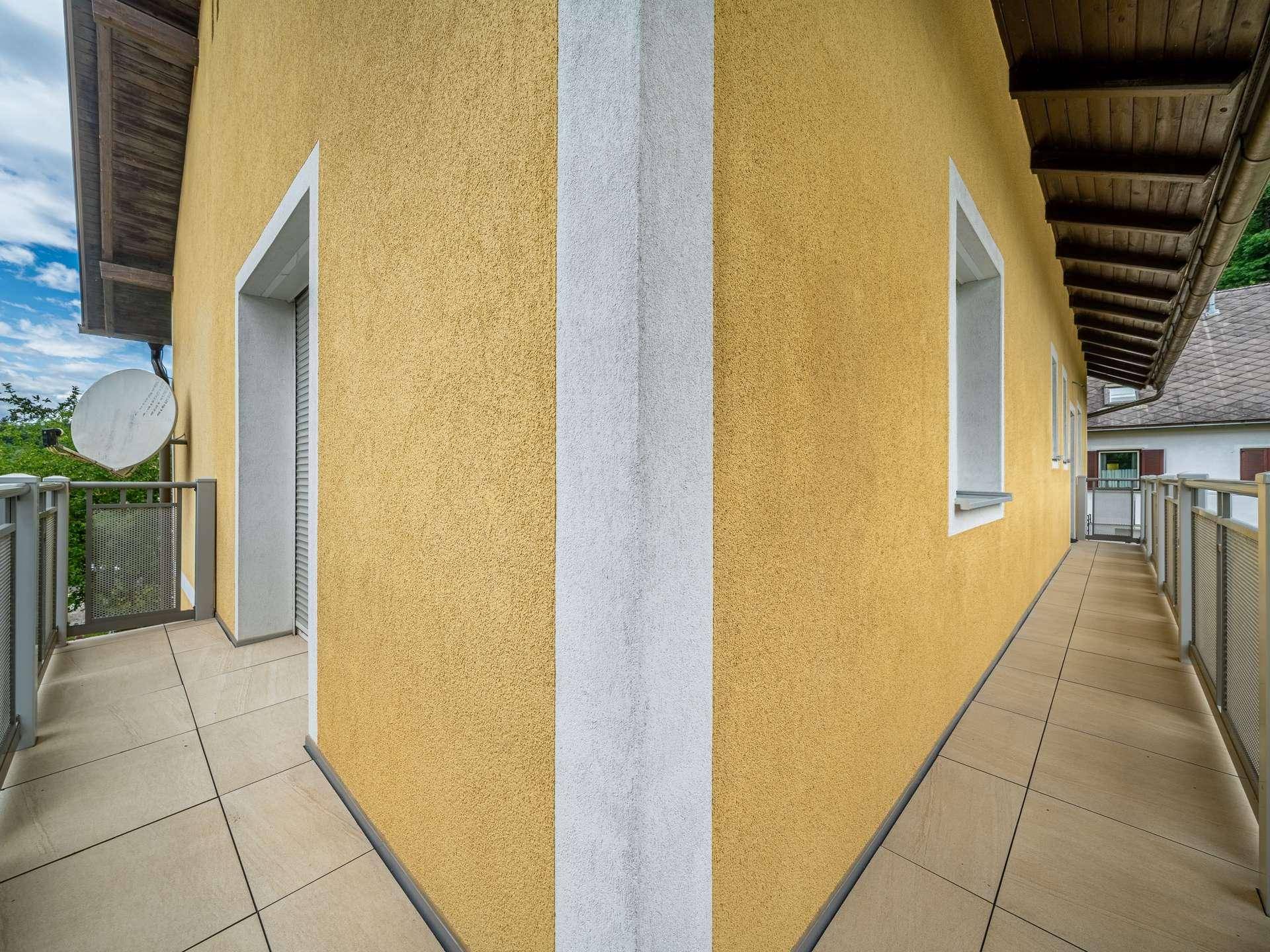 Langer Balkon mit Fliesenboden und gelber Fassade.