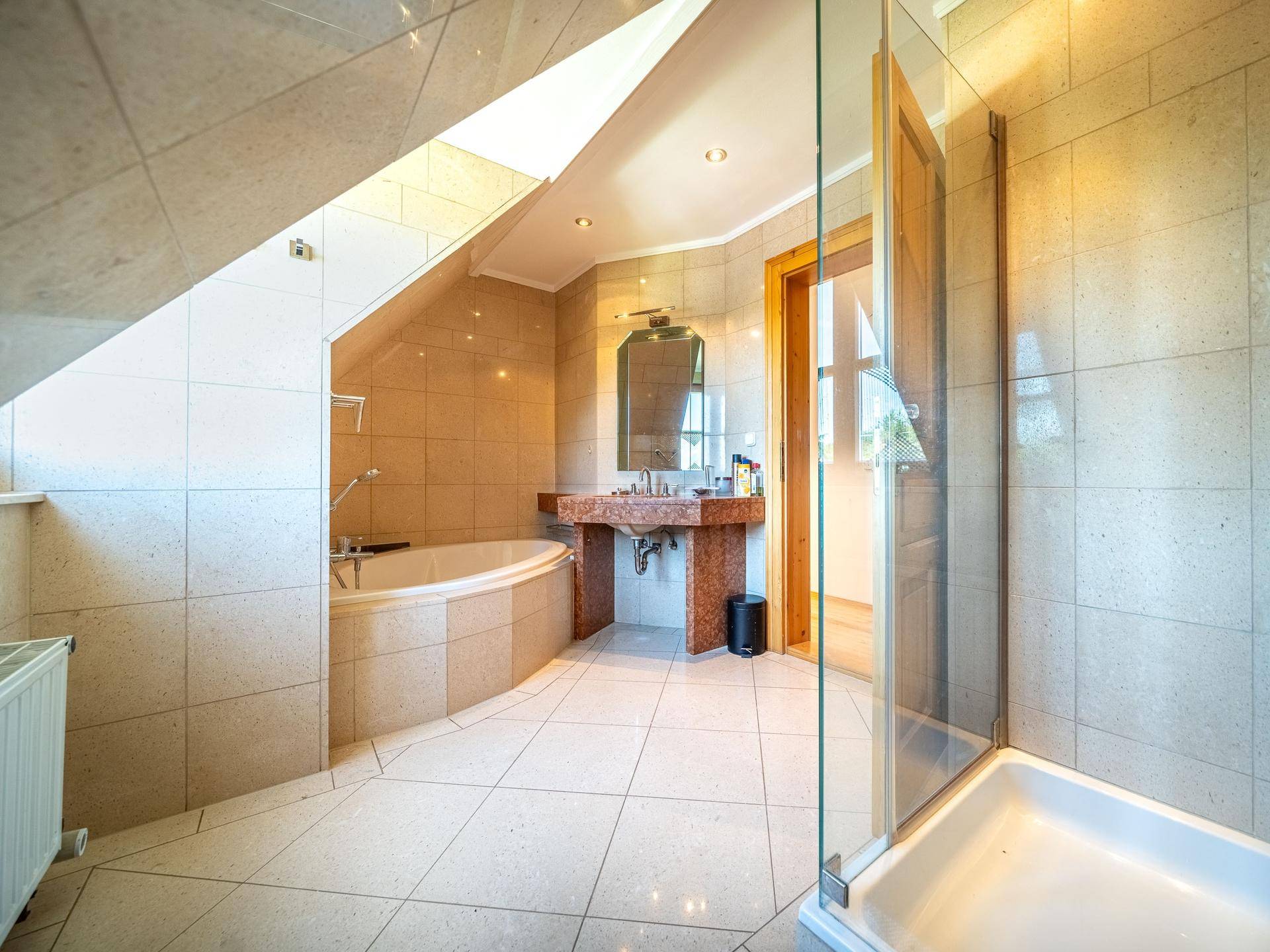 Helles Badezimmer mit beigen Fliesen, Badewanne, Duschkabine und Dachschräge.