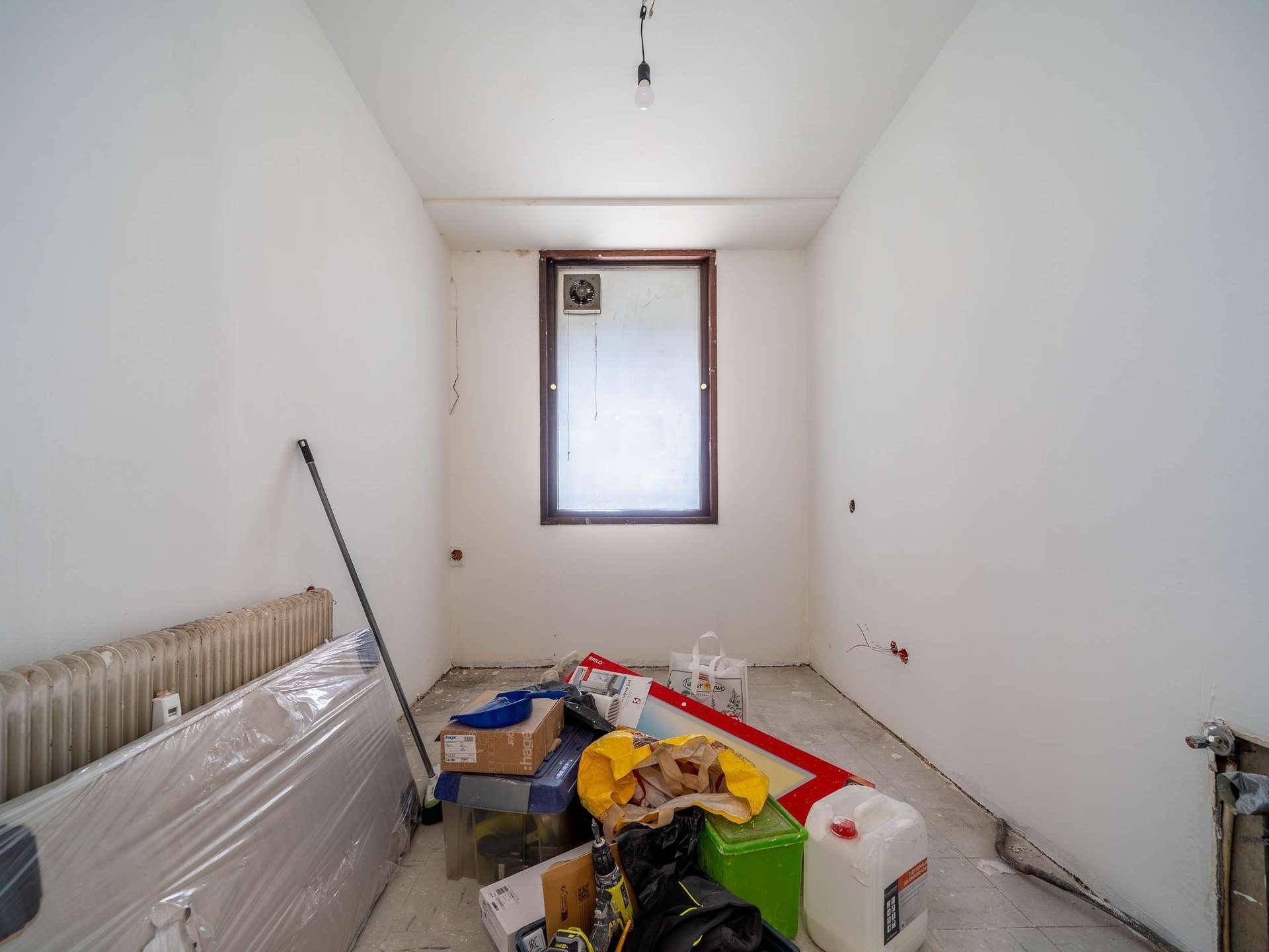 Kleiner Raum in Renovierung mit Fenster, Heizkörper und Baumaterialien, bereit für den Ausbau.