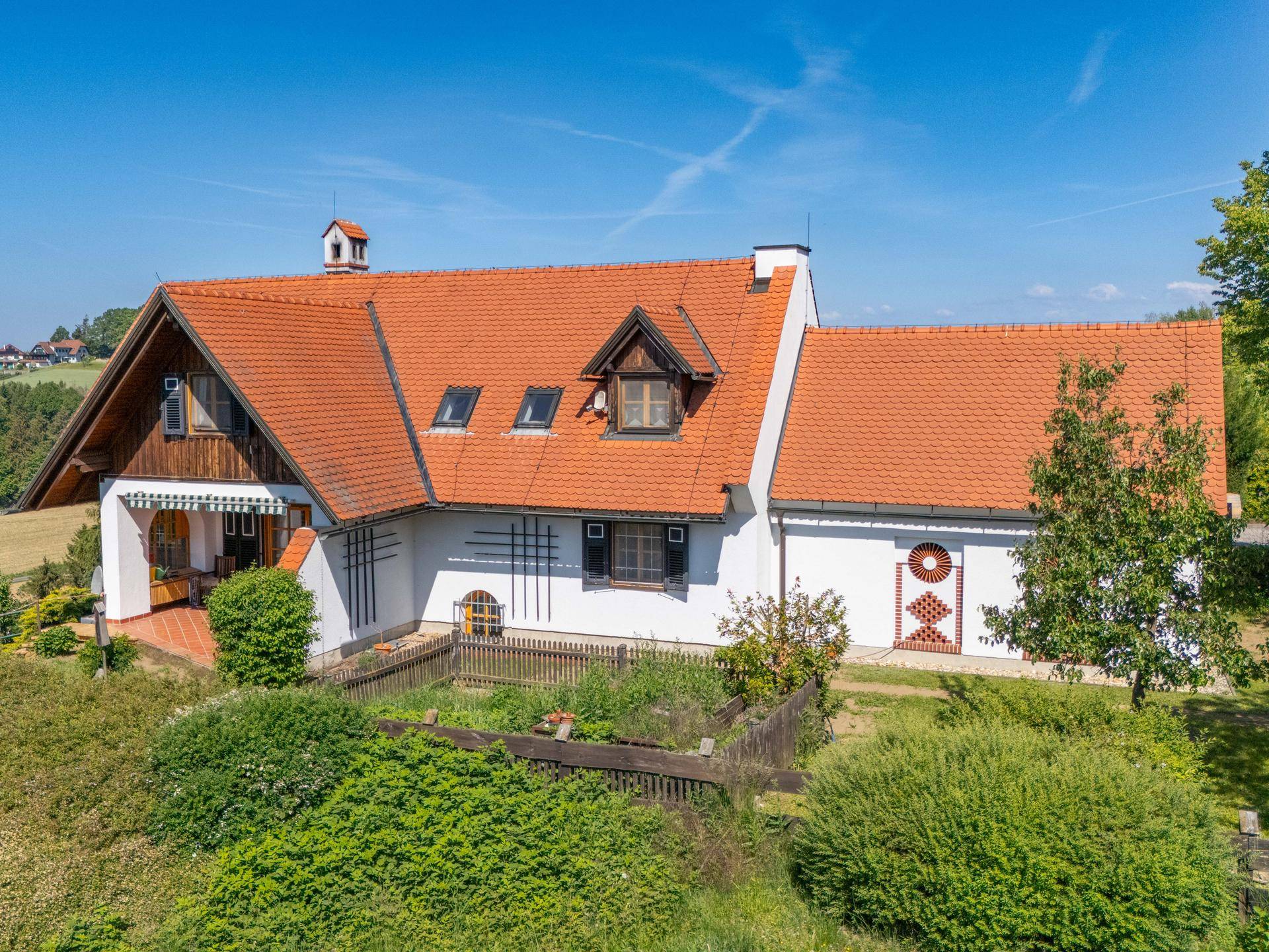 Luftaufnahme des Hauses mit rotem Ziegeldach, weißer Fassade und einem umzäunten Gartenbereich.