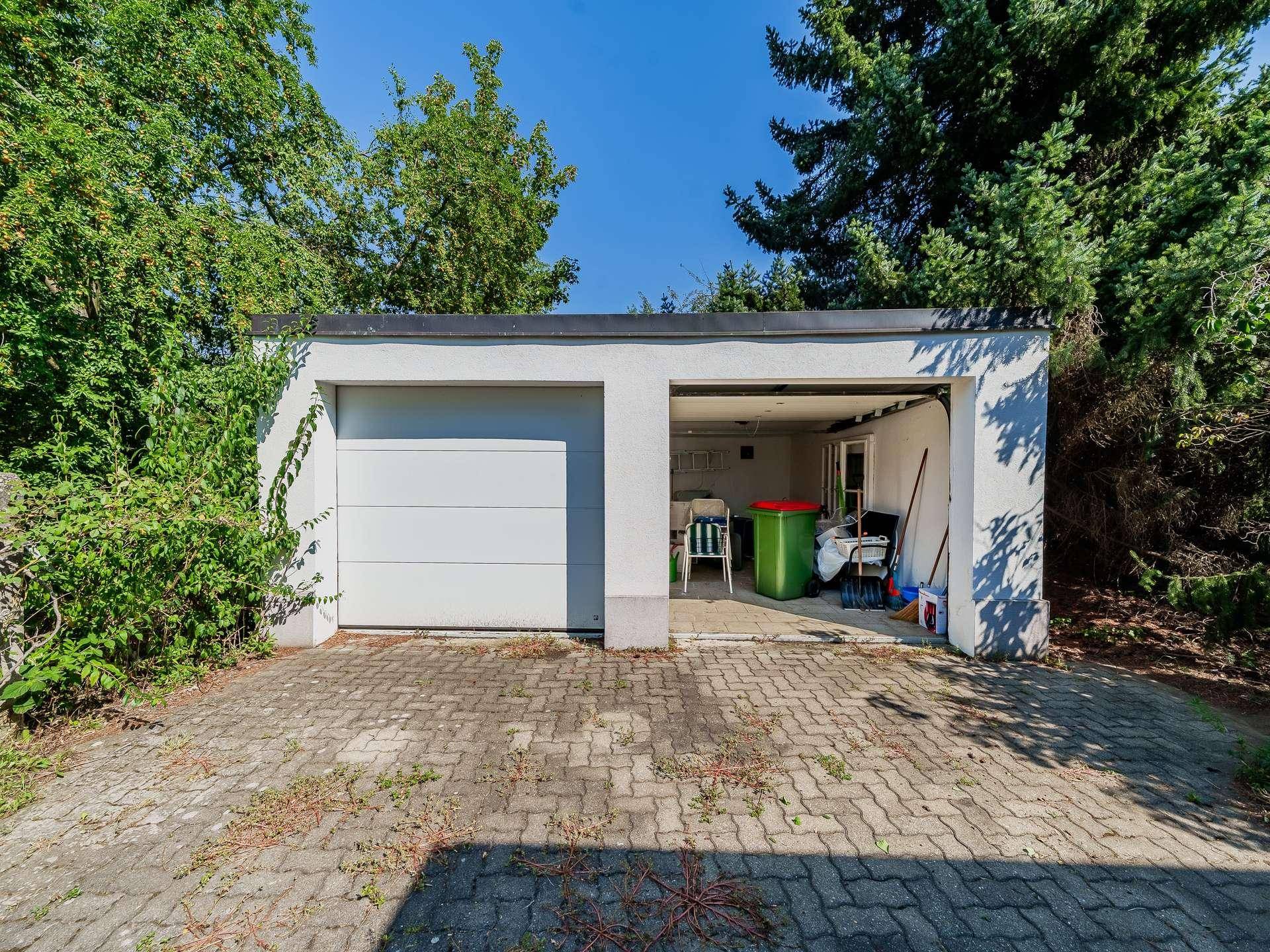 Doppelgarage mit zwei Toren und gepflasterter Zufahrt, umgeben von üppigem Grün.