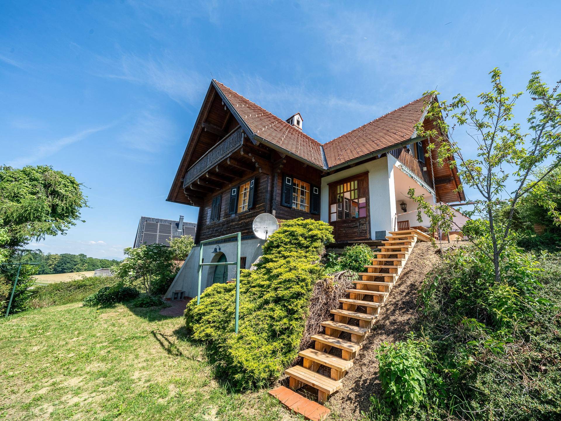 Traditionelles Haus auf einem Hanggrundstück mit Holztreppe und umgebender Natur.