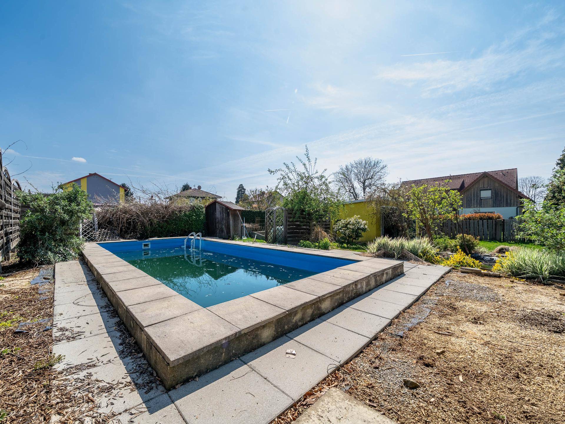 Außenpool im Gartenbereich, umgeben von Steinplatten und Grünflächen.