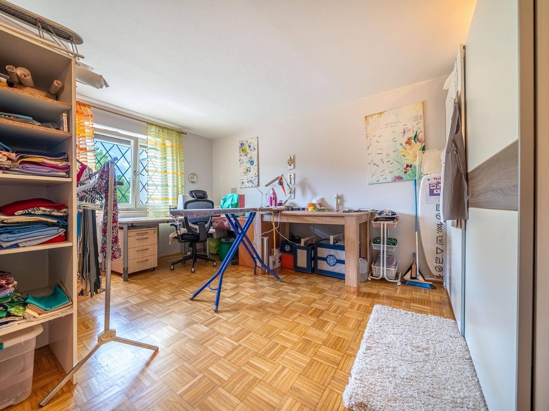 Helles Arbeitszimmer mit Parkettboden, großem Fenster und Regalen, ideal für Hobbys.