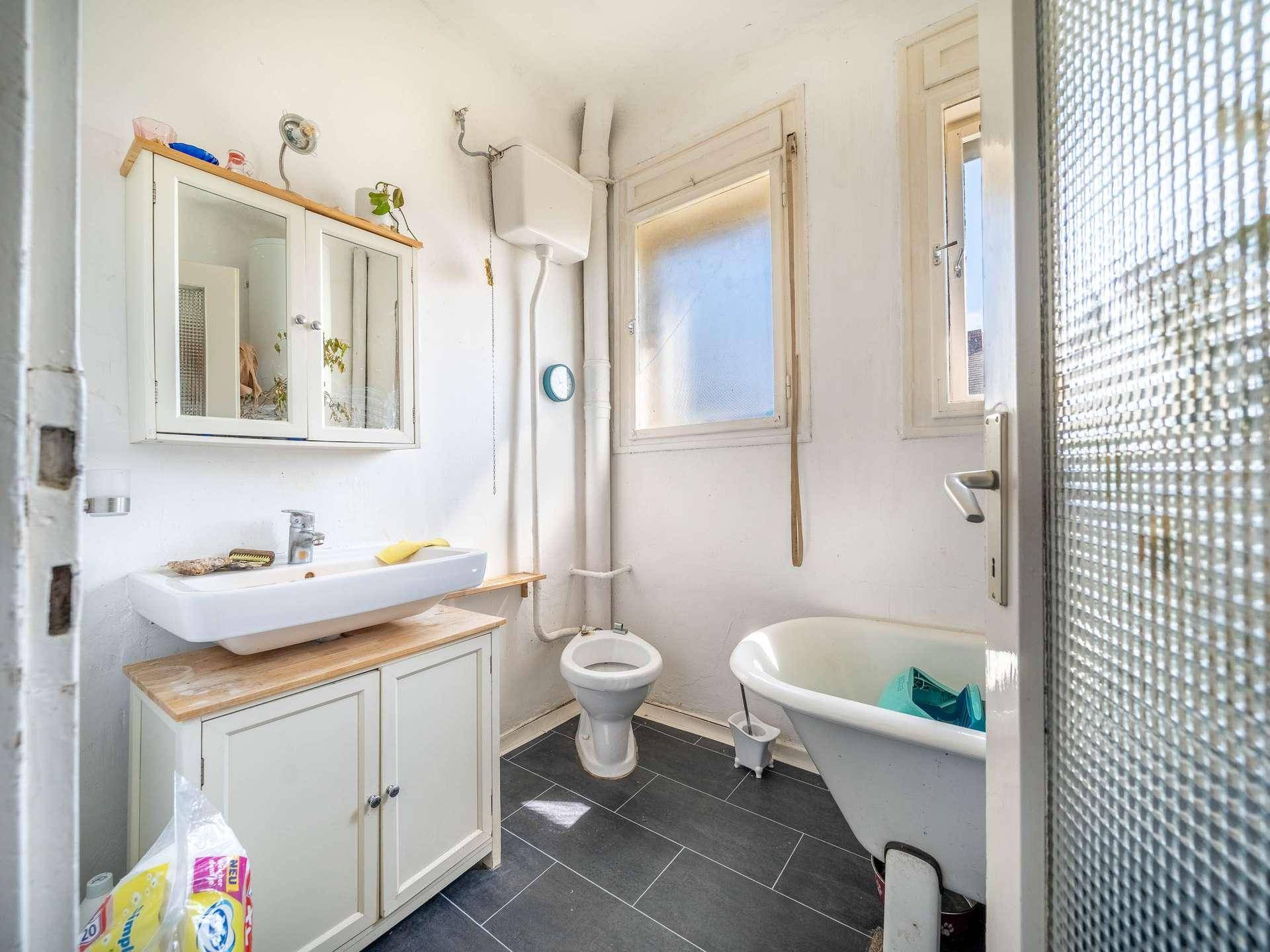 Renoviertes Badezimmer mit dunklen Fliesen, Badewanne und modernem Waschbecken.