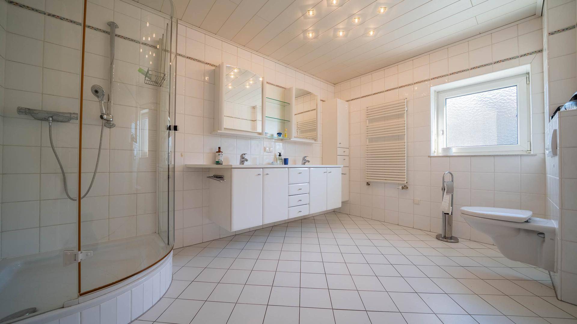 Helles Badezimmer mit Dusche, Doppelwaschbecken, WC und Fenster für Tageslicht.