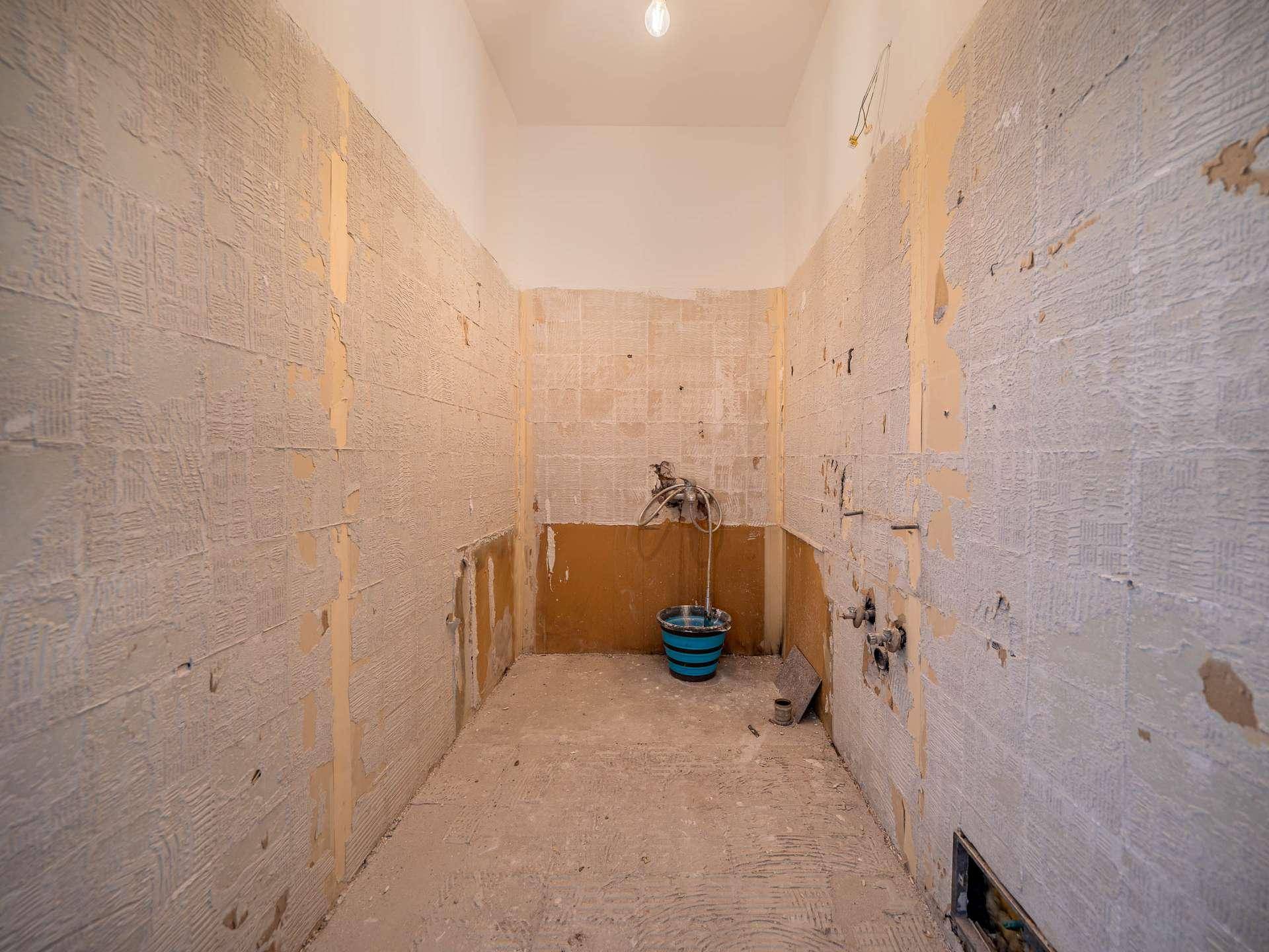 Badezimmer in vollständiger Renovierung mit freigelegten Wänden, Rohren und einem Eimer.