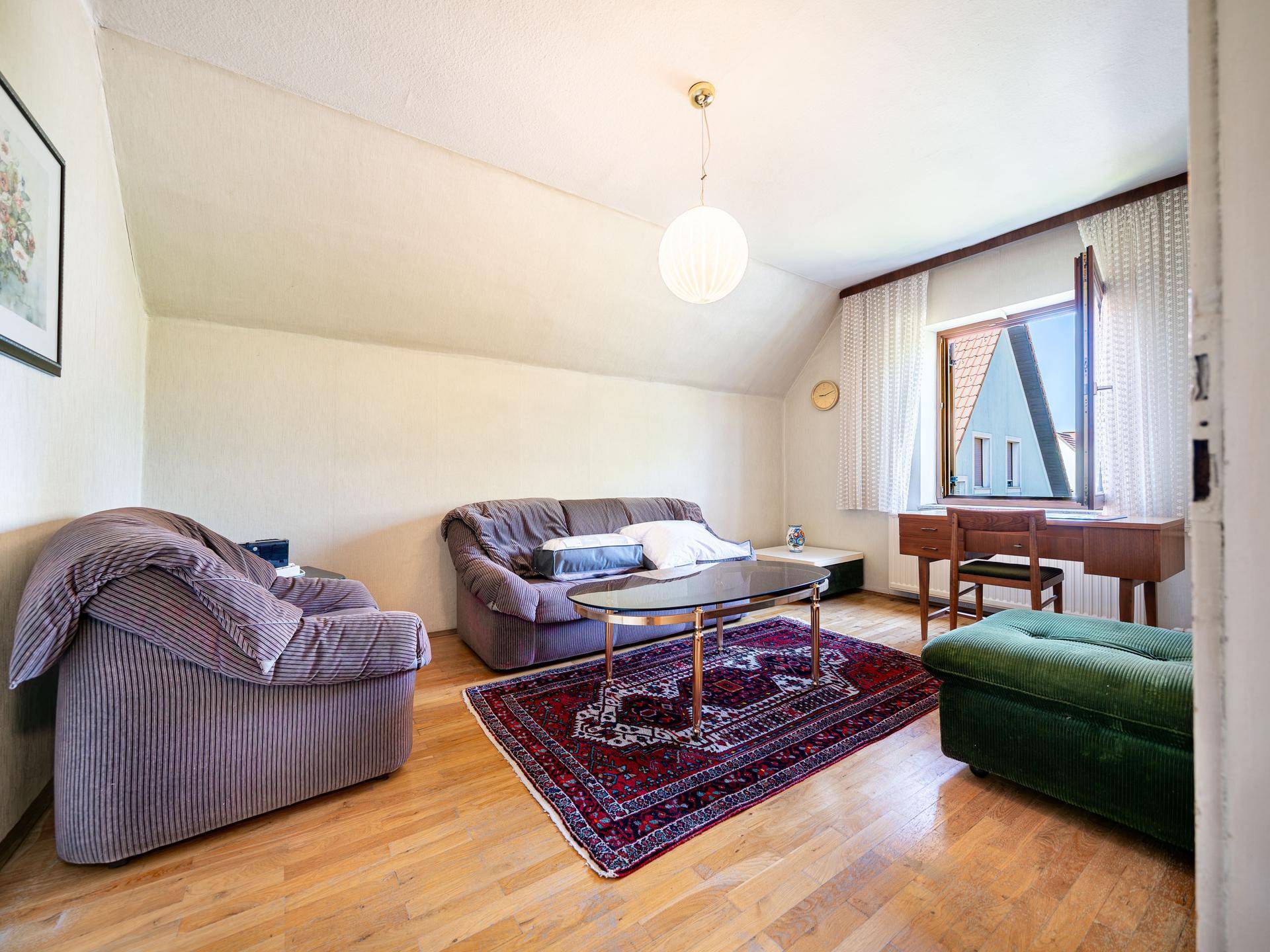 Gemütliches Wohnzimmer im Dachgeschoss mit Schrägen, Sofa und Teppich.