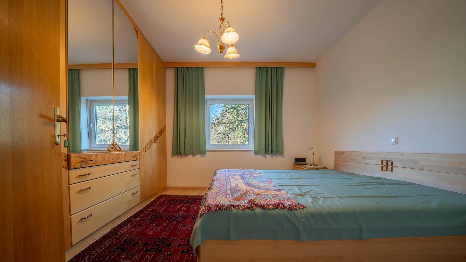 Schlafzimmer mit Holzbett, Teppich und Fenster für natürliches Licht.