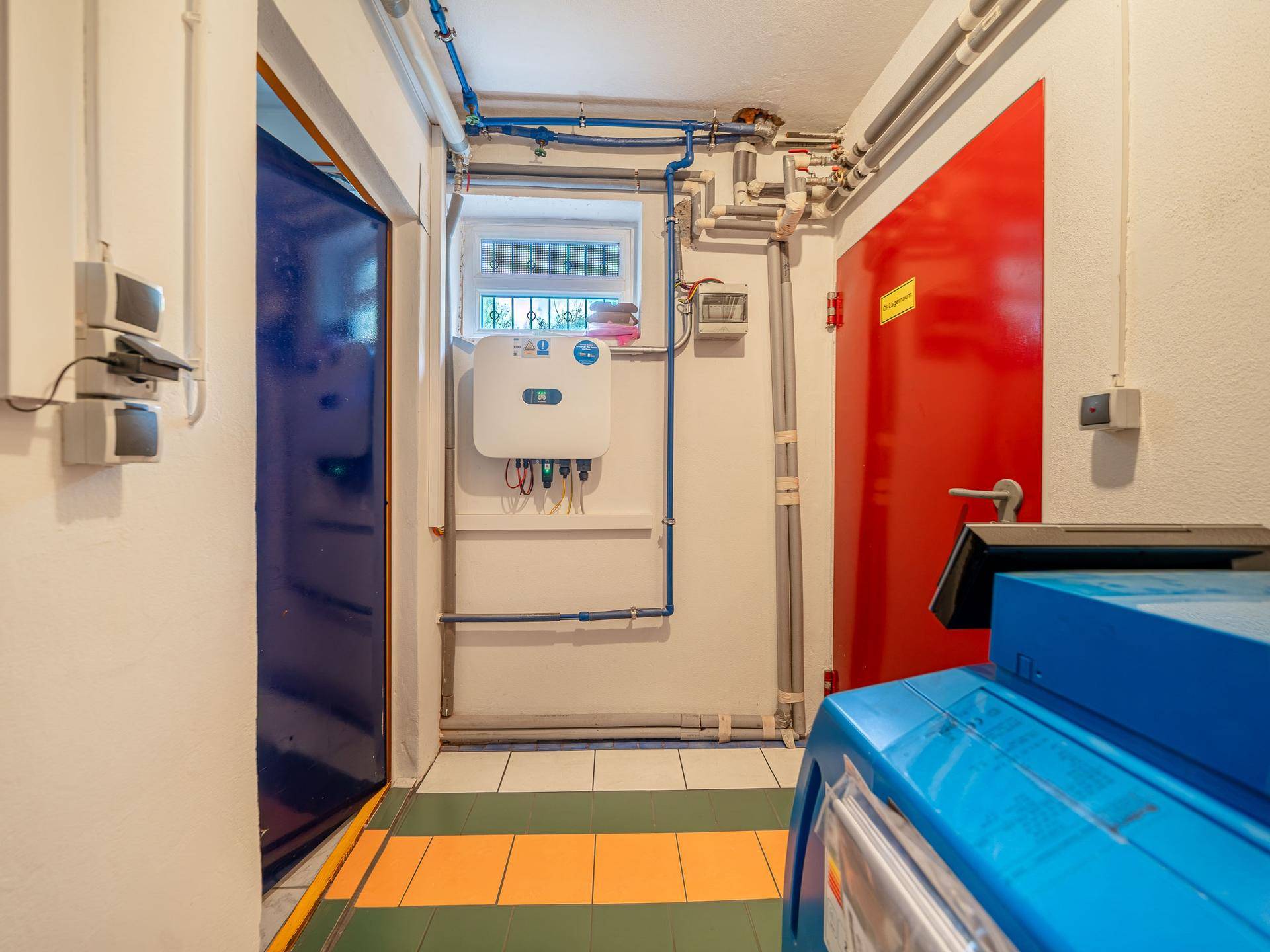 Technikraum mit Fenster, sichtbaren Rohren und elektrischen Installationen, gut organisiert.