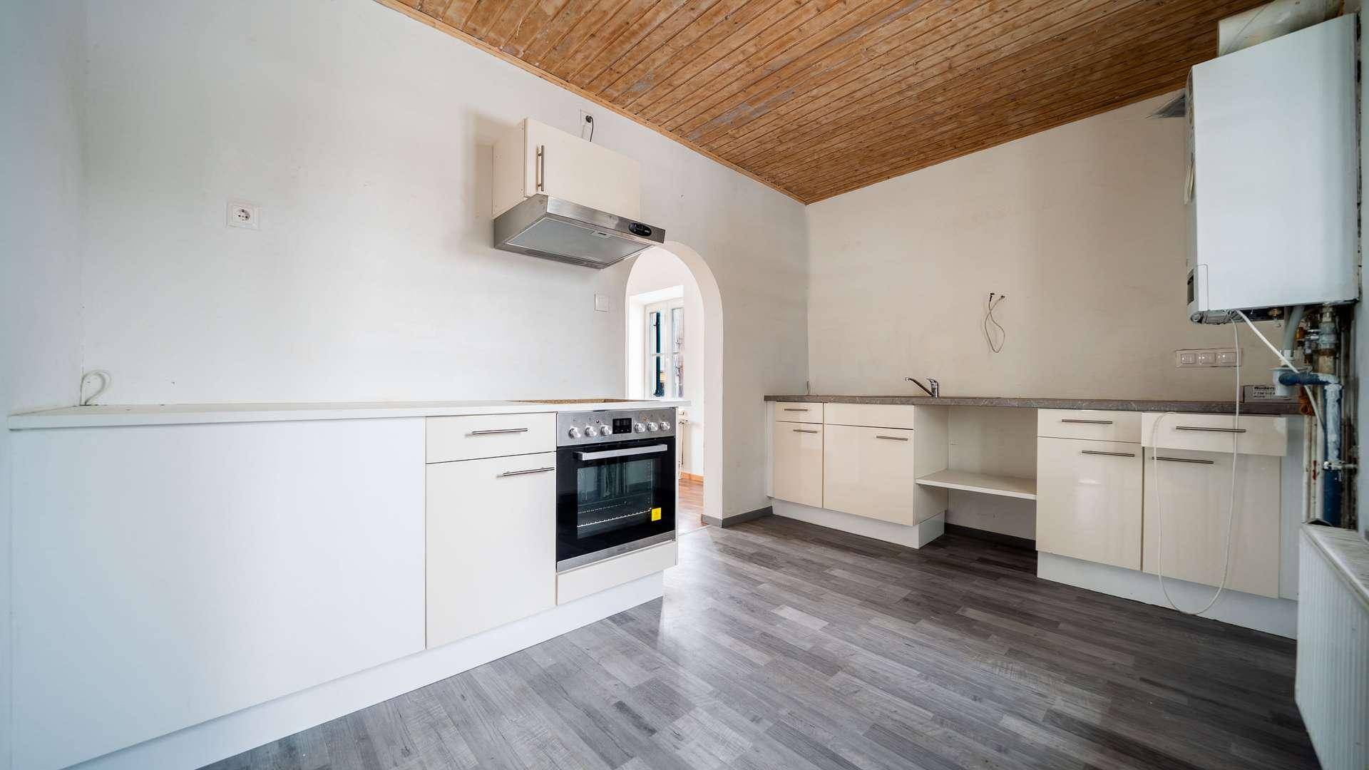 Helle Küche mit Holzbalkendecke, Laminatboden und Bogenöffnung zu einem weiteren Raum.