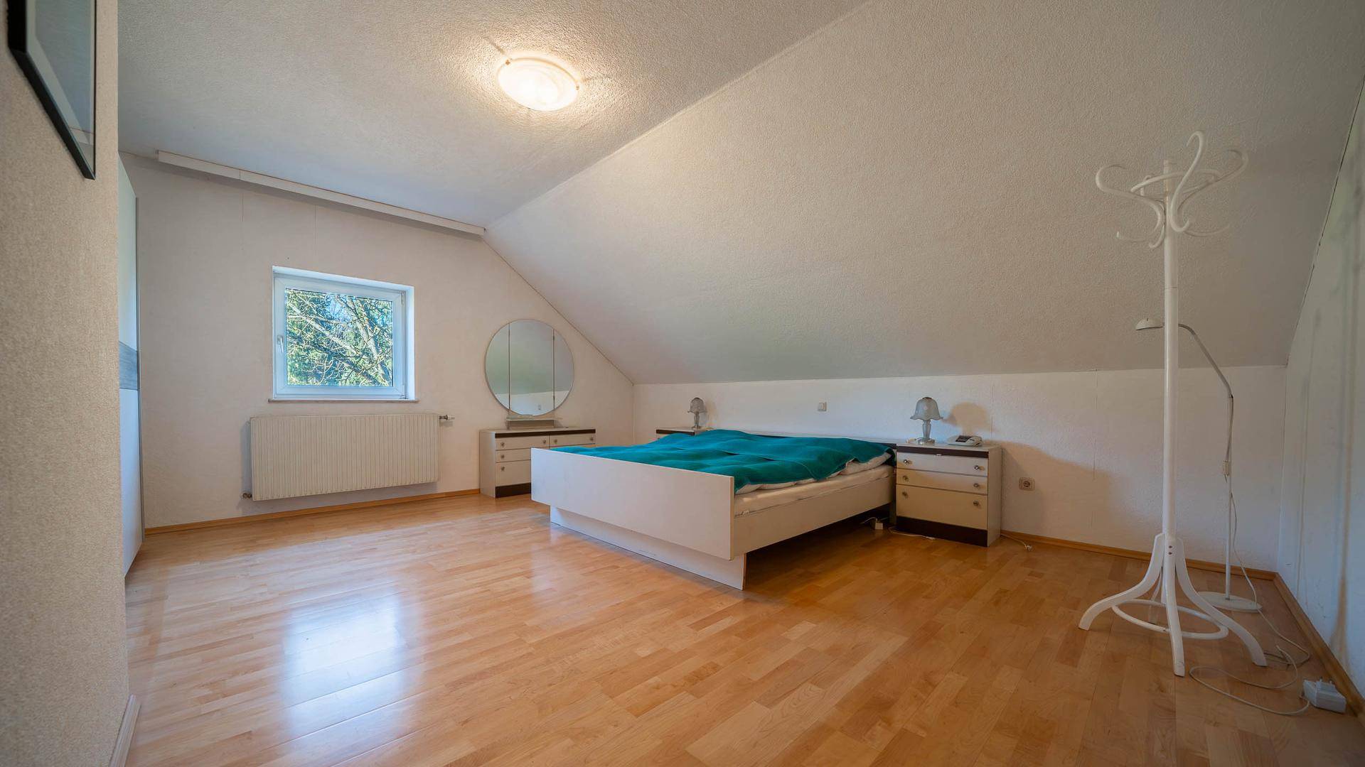 Geräumiges Schlafzimmer im Dachgeschoss mit Holzboden, Dachschräge und Fensterblick ins Grüne.