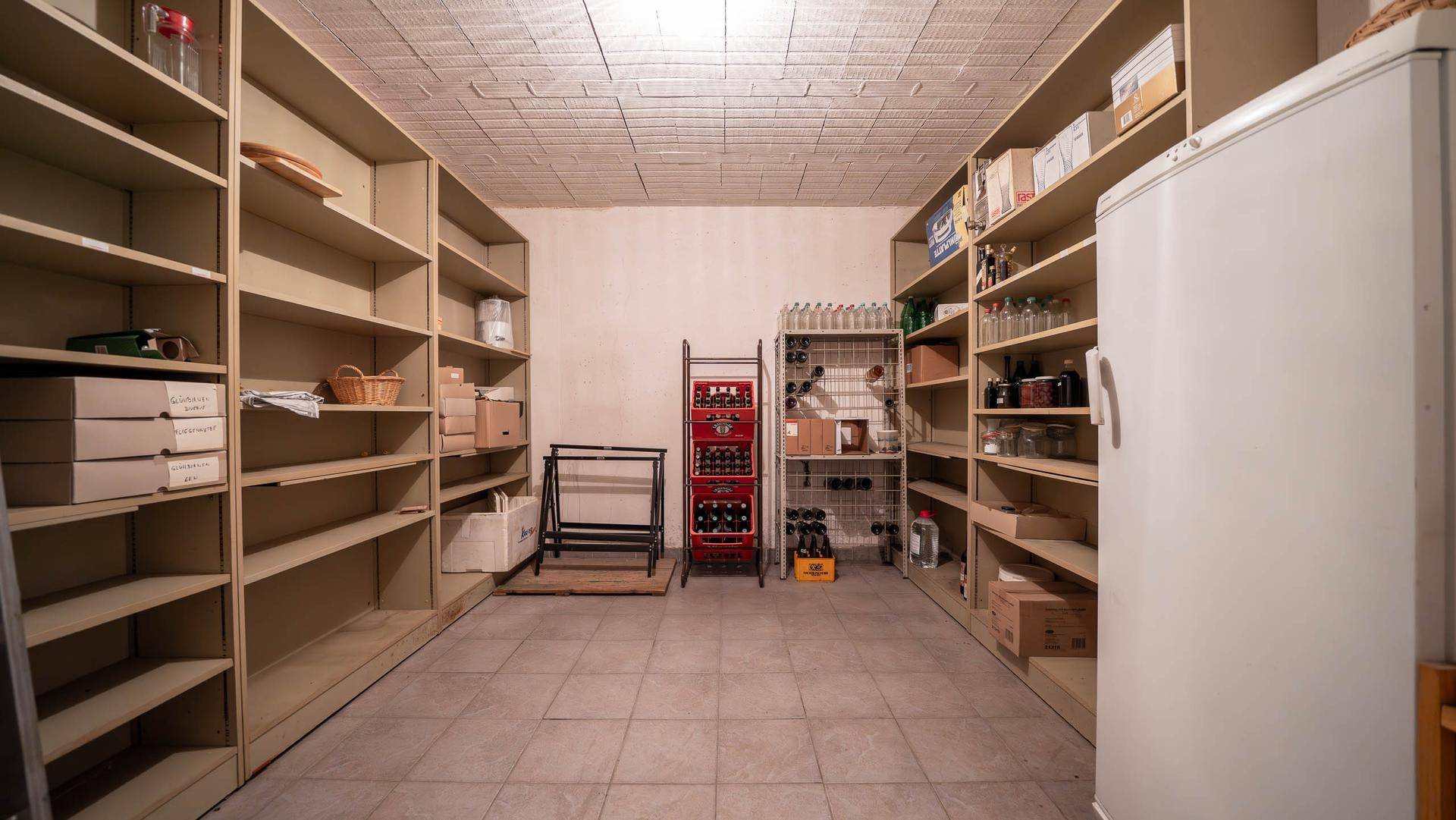 Geräumiger Weinkeller mit vielen Regalen, Flaschen und einem Kühlschrank.