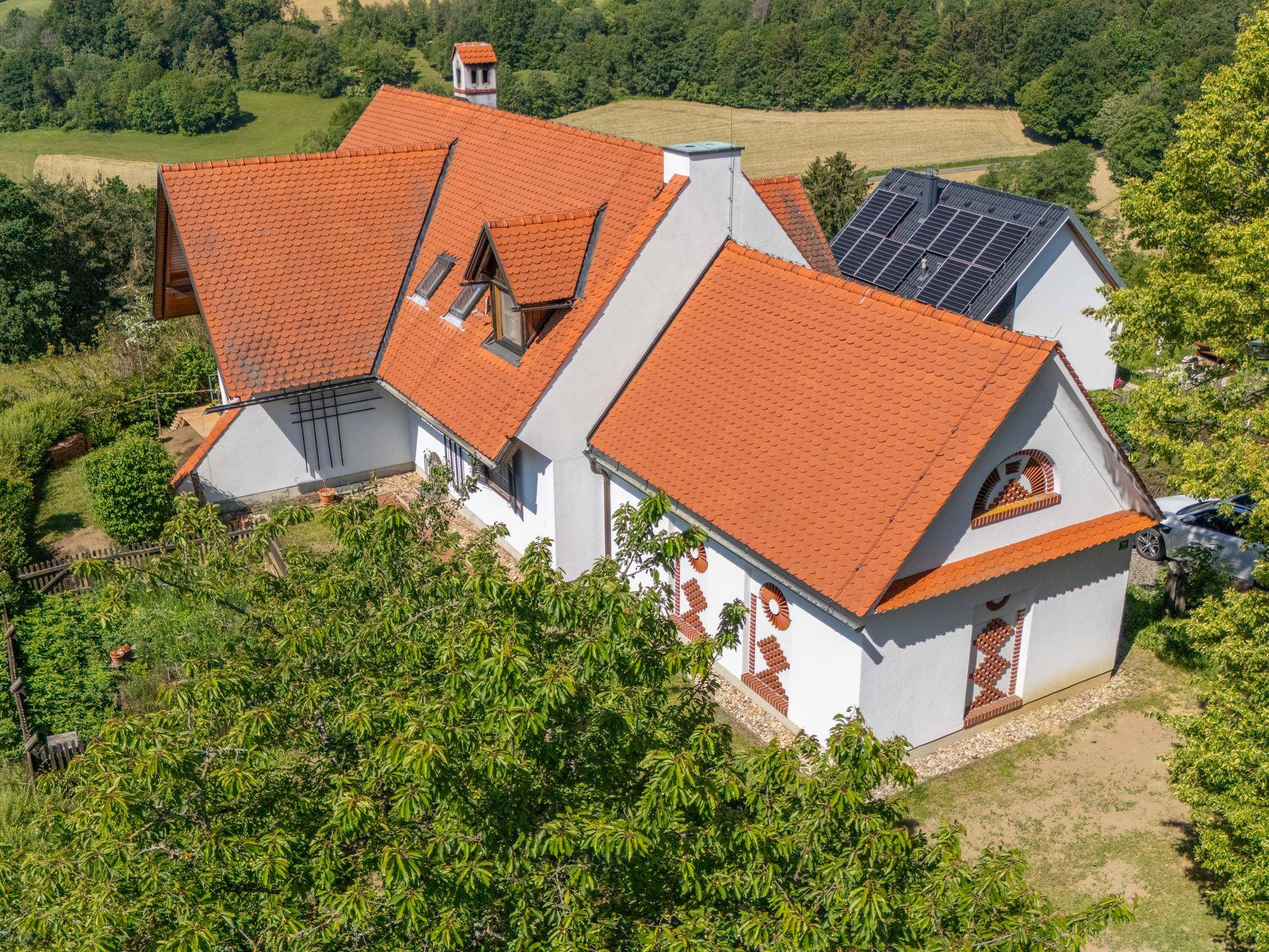 Luftaufnahme der Rückseite des Hauses mit rotem Ziegeldach und Photovoltaikanlage auf Nachbargebäude.