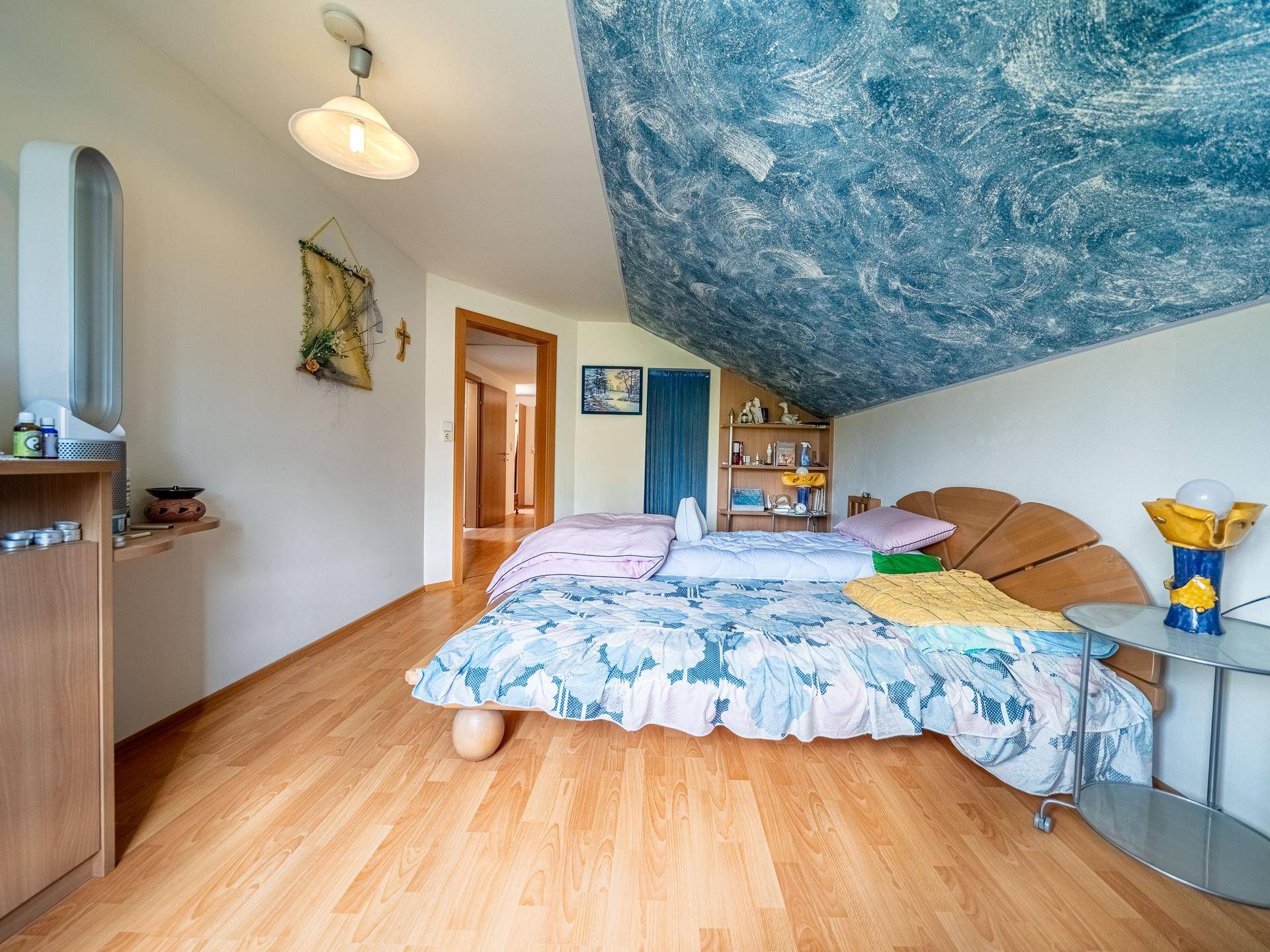 Dachgeschoss-Schlafzimmer mit Holzbett, Laminatboden und blauer Deckenverzierung.