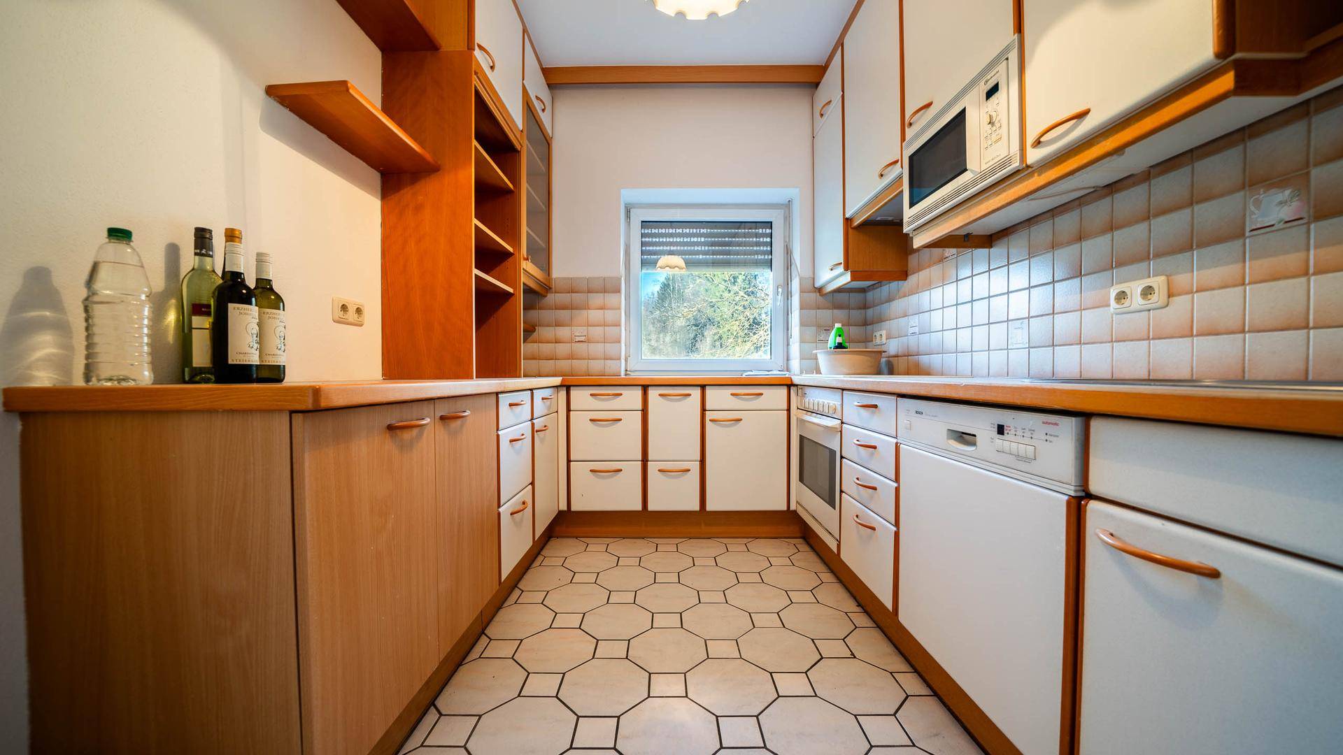 Funktionale Küche mit Holz- und weißen Schränken, Fliesenboden und Fensterblick.