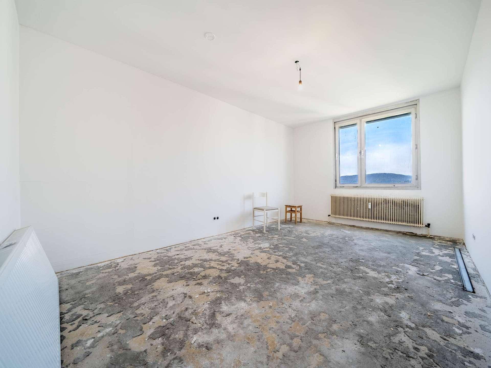 Helles, leeres Zimmer in Renovierung mit großem Fenster und weitem Blick ins Grüne.