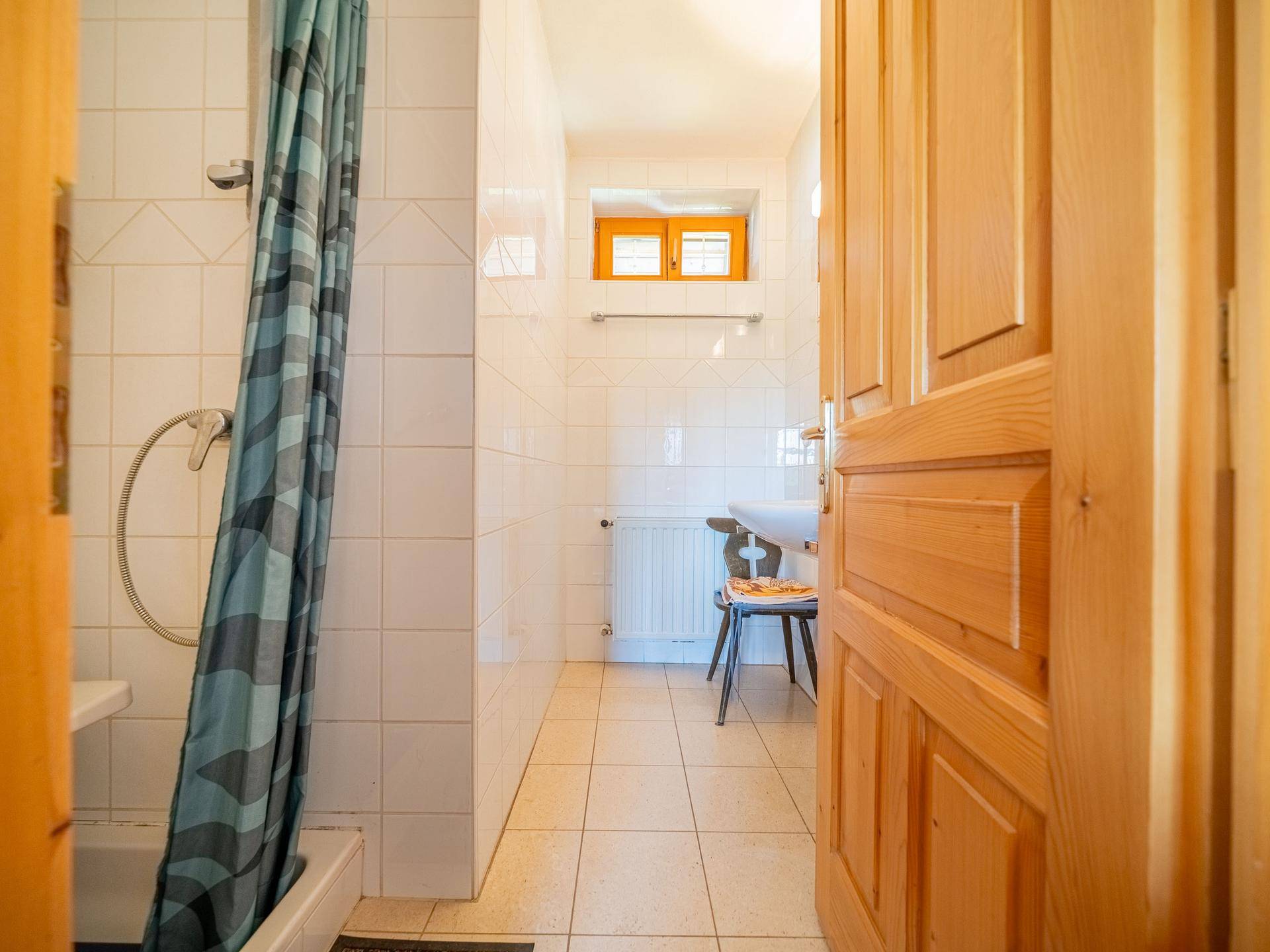 Kleines Badezimmer mit weißen Fliesen, Duschwanne und Fenster für Tageslicht.