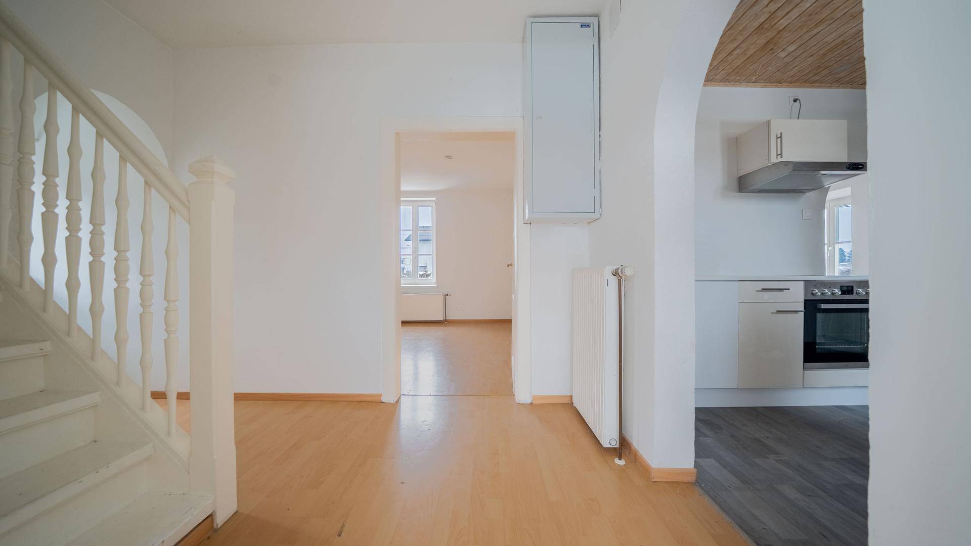 Heller Flur mit Holztreppe und Zugang zu Küche und Wohnbereich, mit hellem Holzboden.