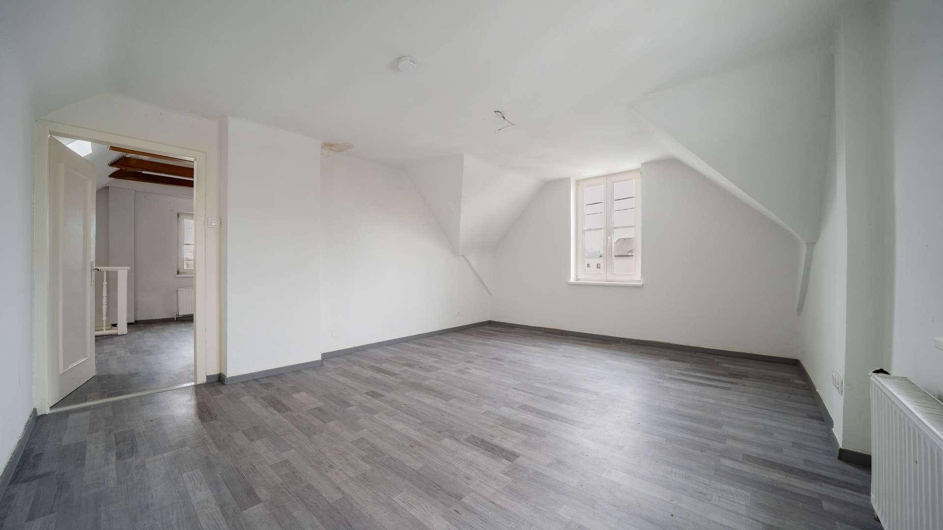 Geräumiges Dachzimmer mit schrägen Wänden, Fenster und grauem Laminatboden.