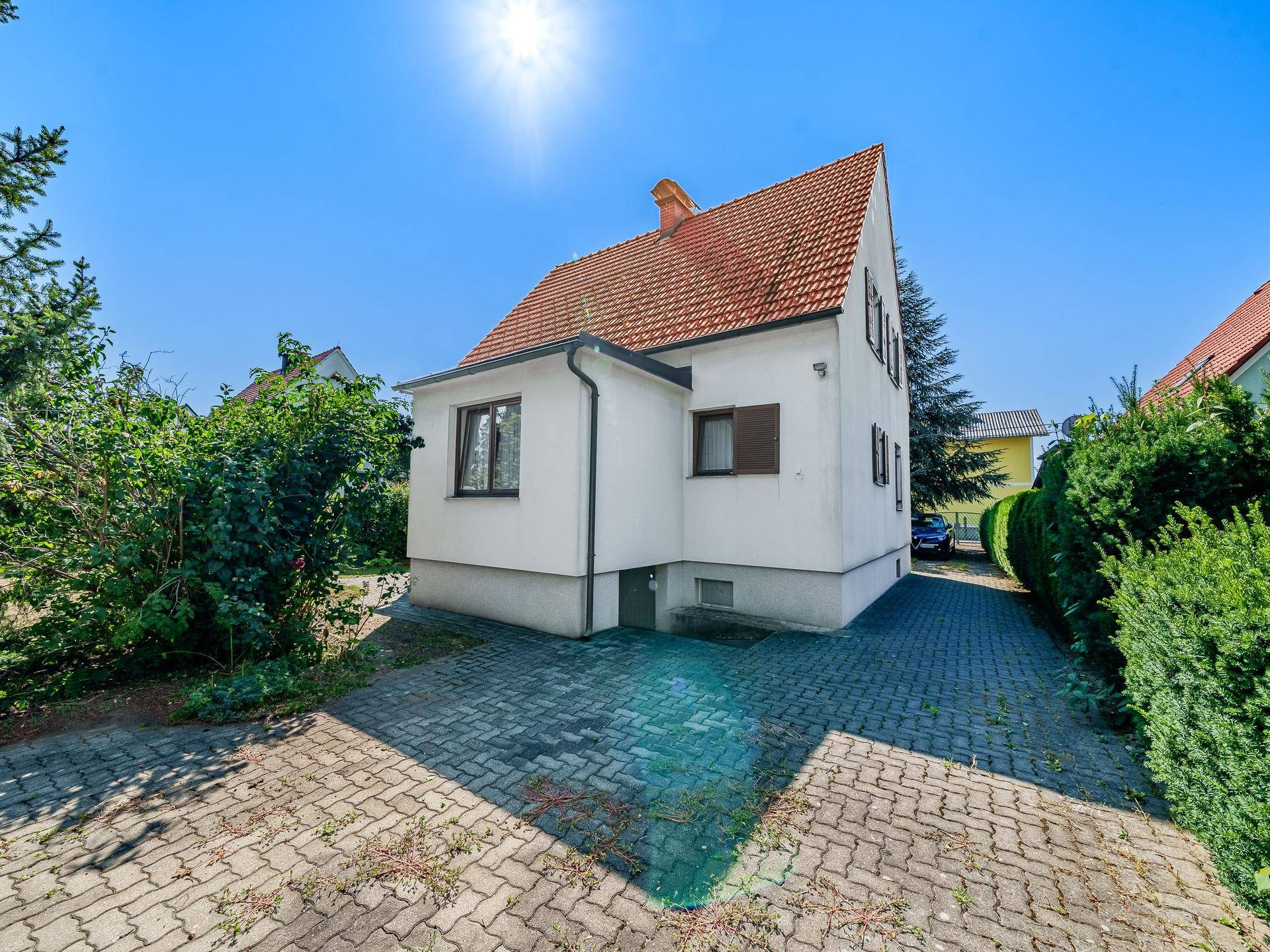 Seitenansicht des Hauses mit gepflasterter Zufahrt und umgebender Grünfläche.
