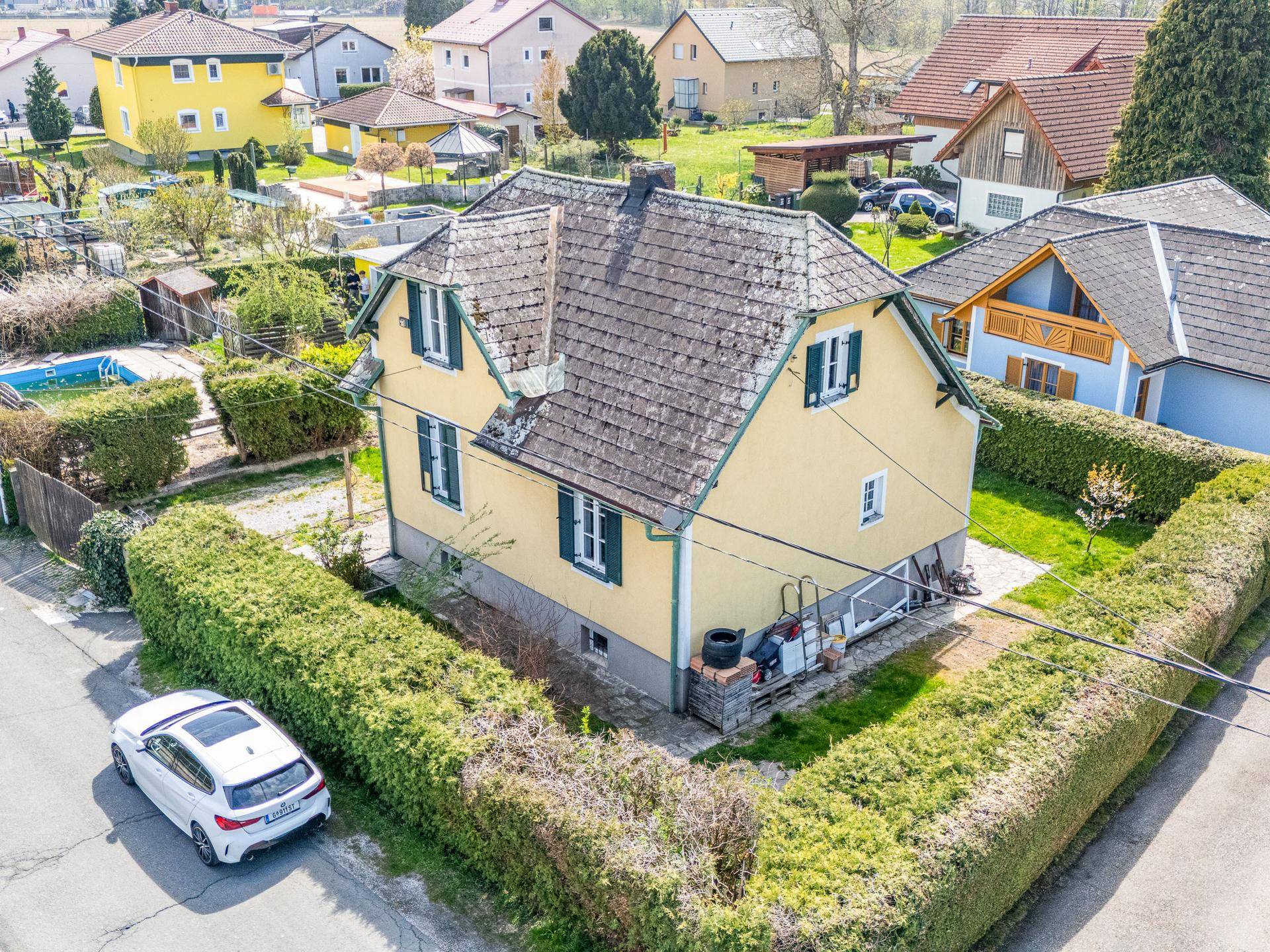 Vogelperspektive des Hauses mit gepflegtem Garten, Hecken und angrenzender Straße mit parkendem Auto.