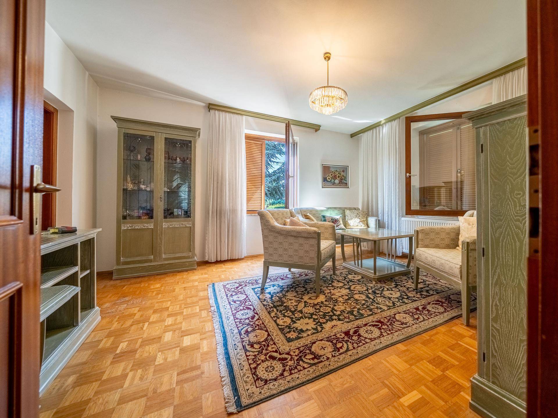 Helles Wohnzimmer mit Parkettboden, traditionellem Teppich und Blick in den Garten.