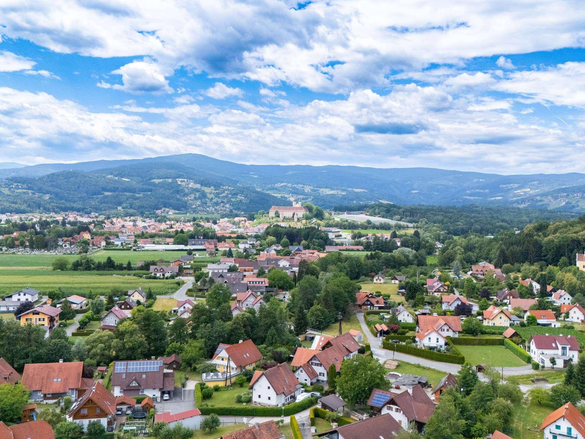 Panoramische Luftaufnahme einer Siedlung mit vielen Häusern, Feldern und Bergen.