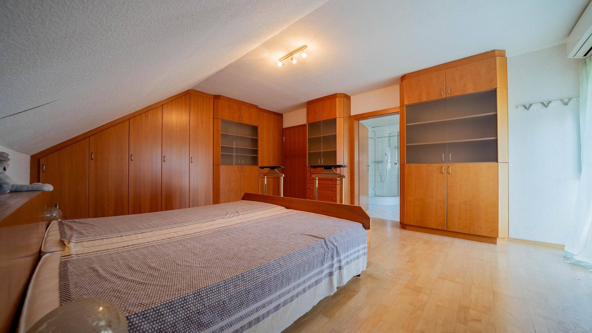 Geräumiges Schlafzimmer mit Holzboden, Dachschräge und umfangreichen Holz-Einbauschränken.