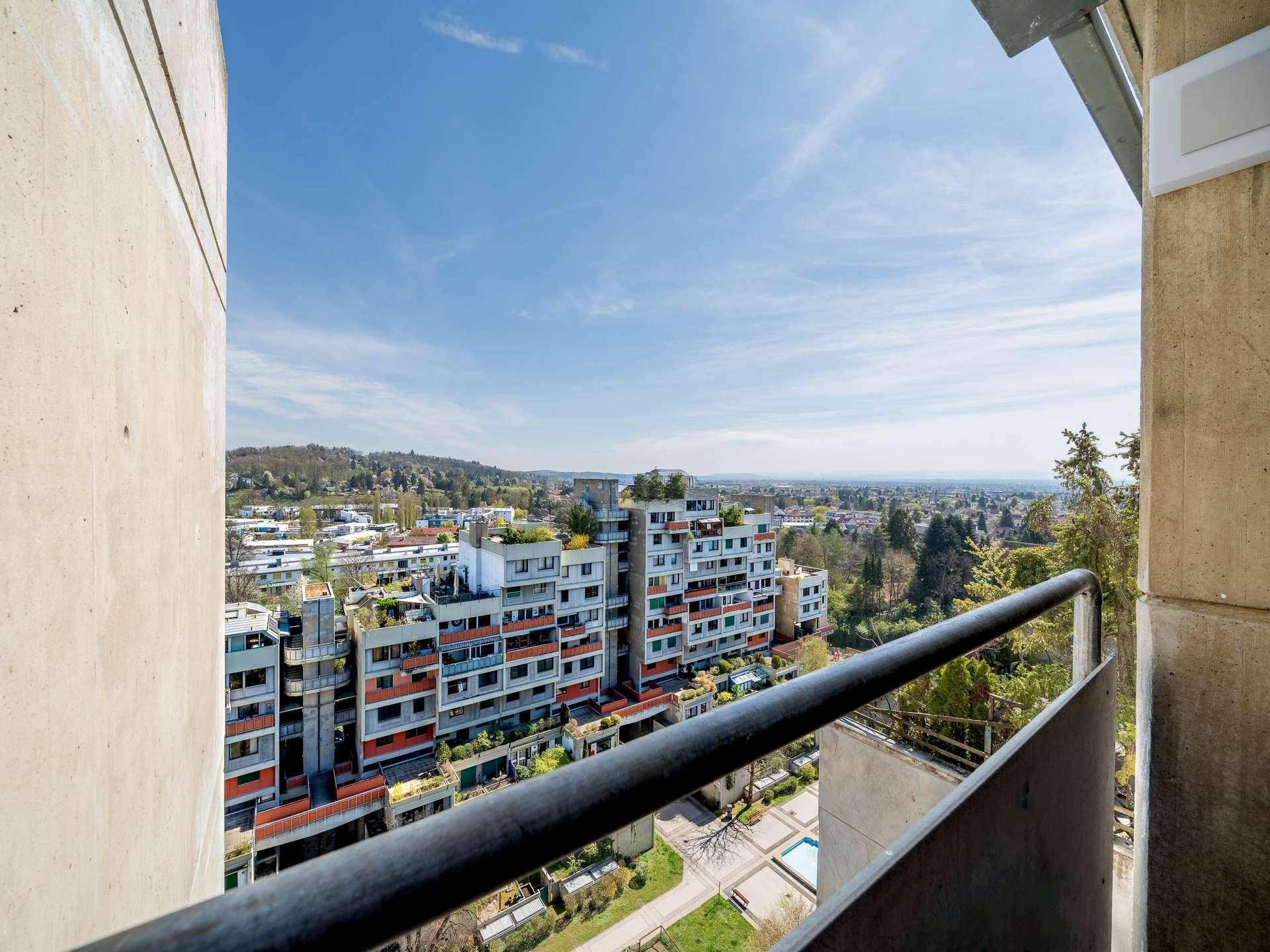 Balkon mit Metallgeländer und weitem Blick über die umliegende Wohnsiedlung und Landschaft.