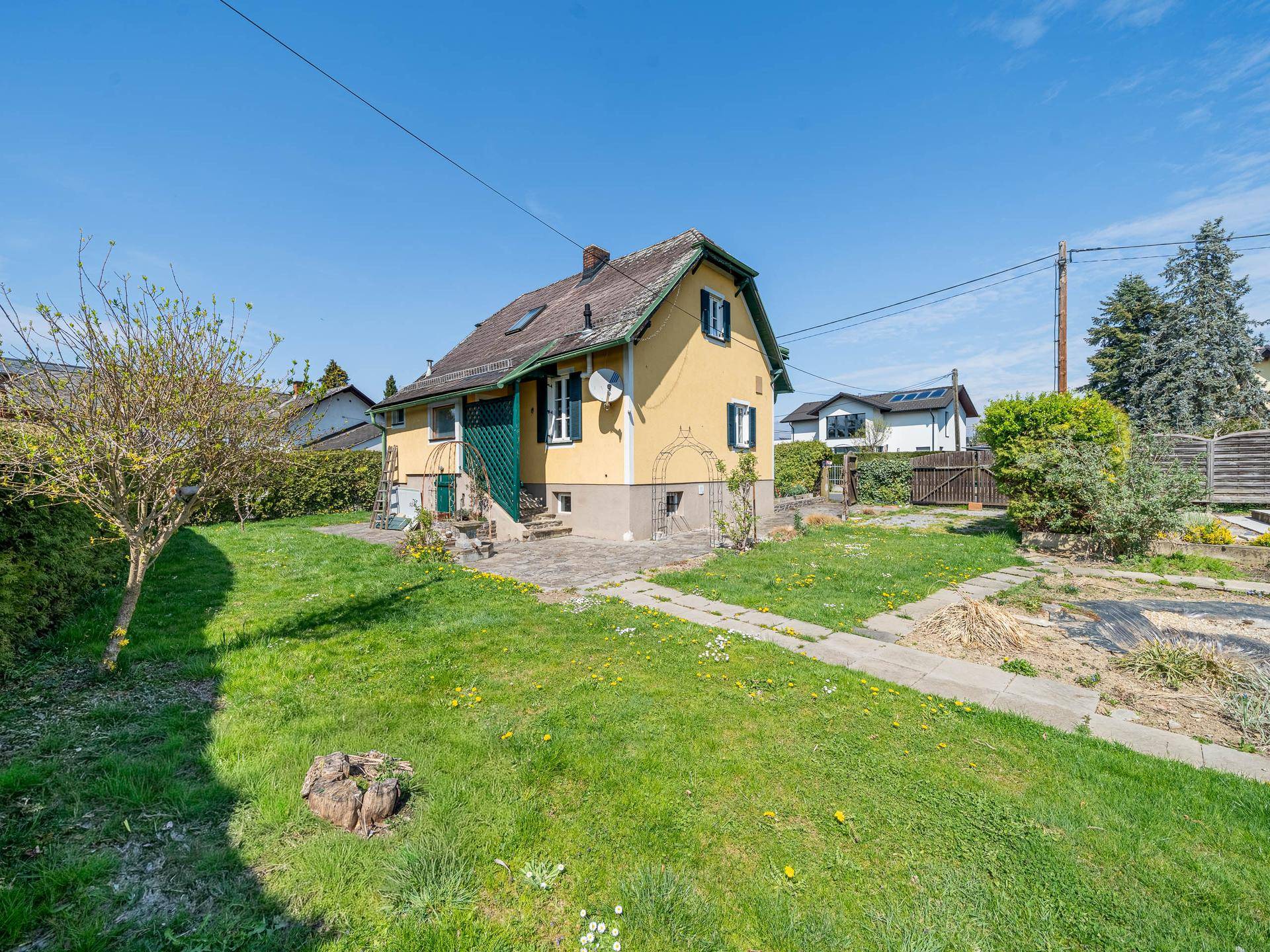 Blick auf das gelbe Haus mit Garten und Rasenfläche an einem sonnigen Tag.