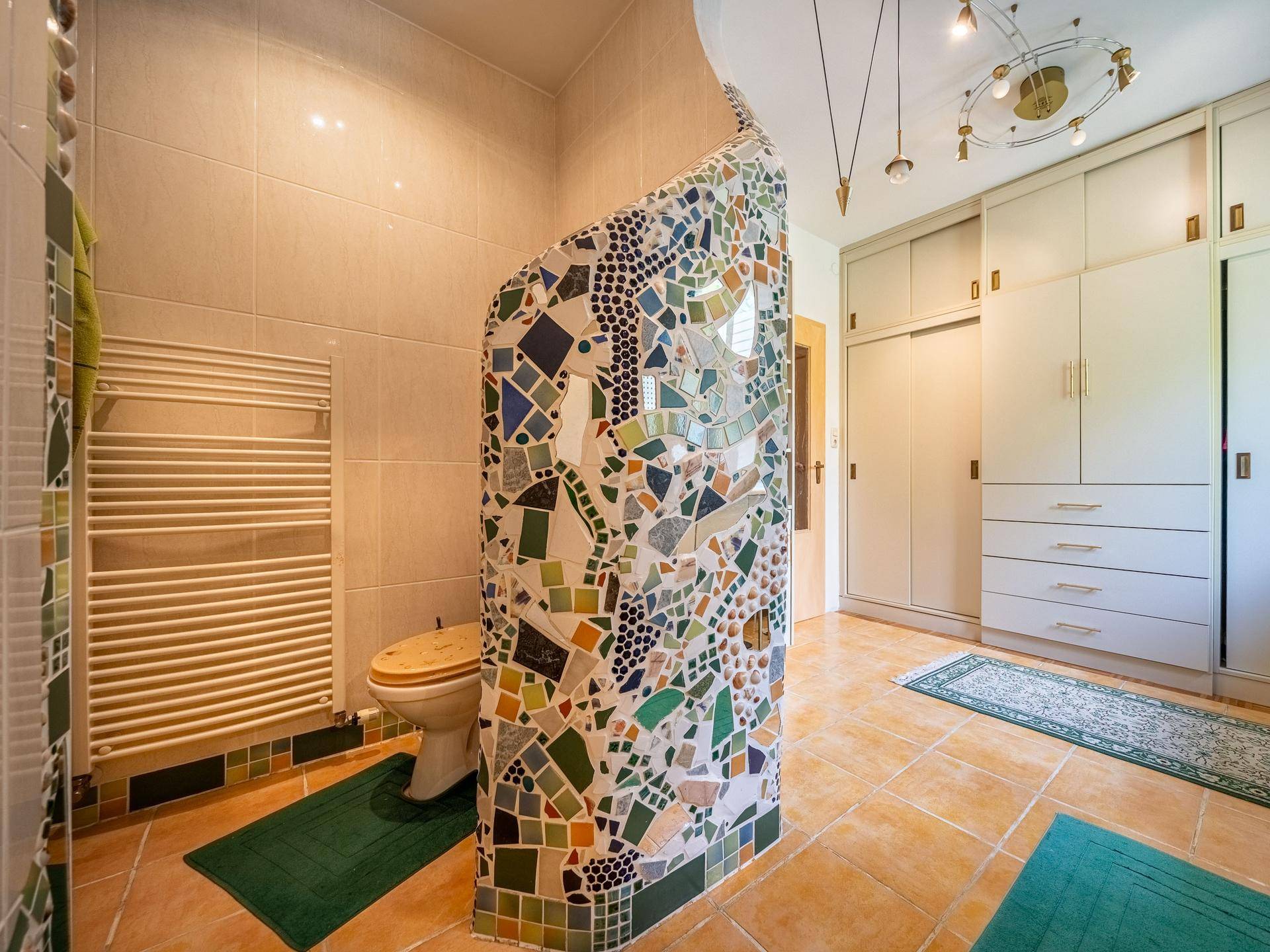 Badezimmer mit WC, Mosaikwand, Fliesenboden und integrierten Schränken.