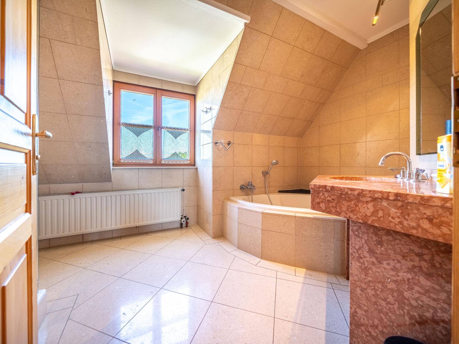 Geräumiges Badezimmer mit beigen Fliesen, Badewanne und Fenster unter der Dachschräge.