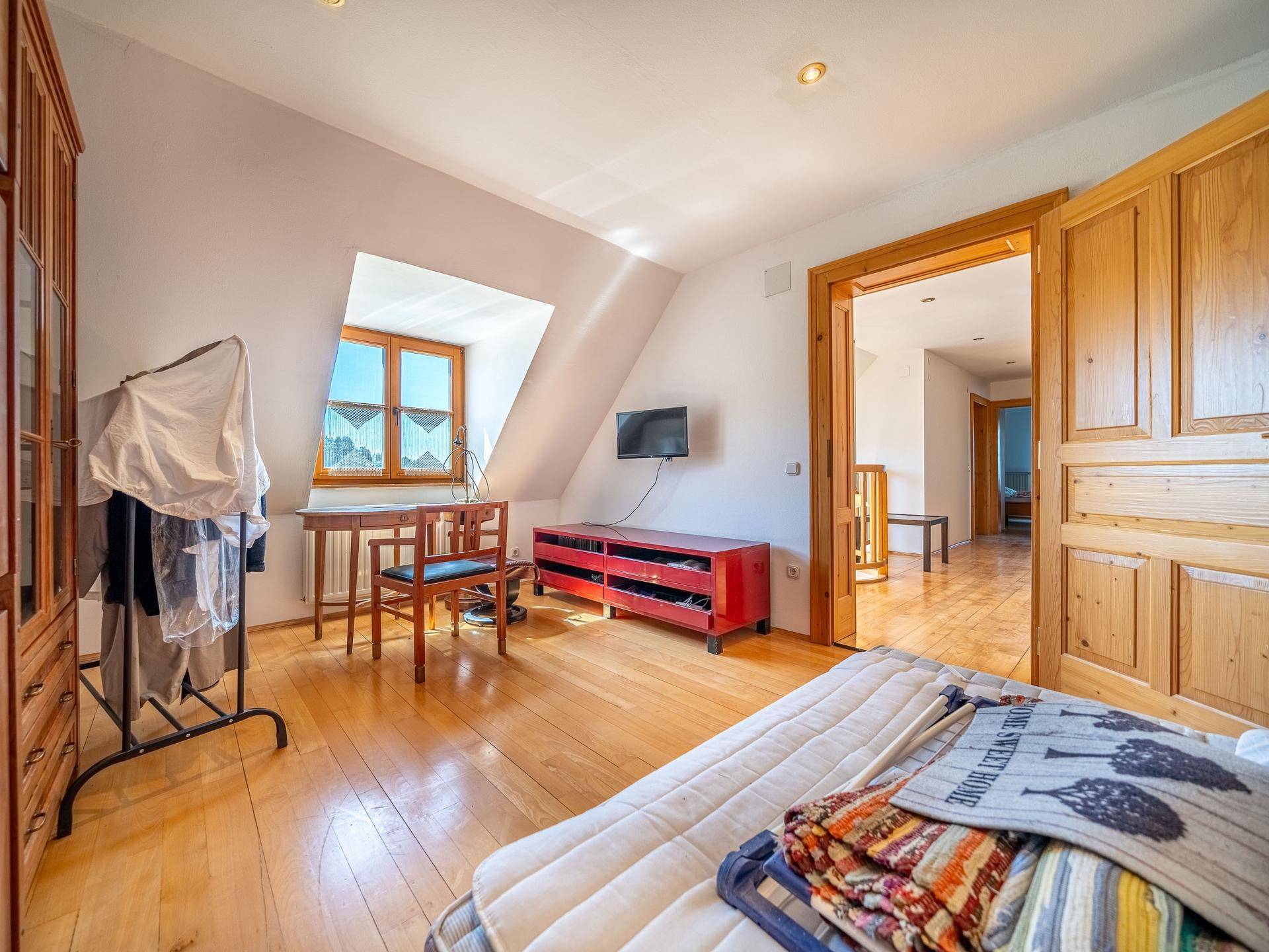 Dachgeschoss-Schlafzimmer mit Holzfußboden, Schreibtisch und Blick aus dem Fenster.